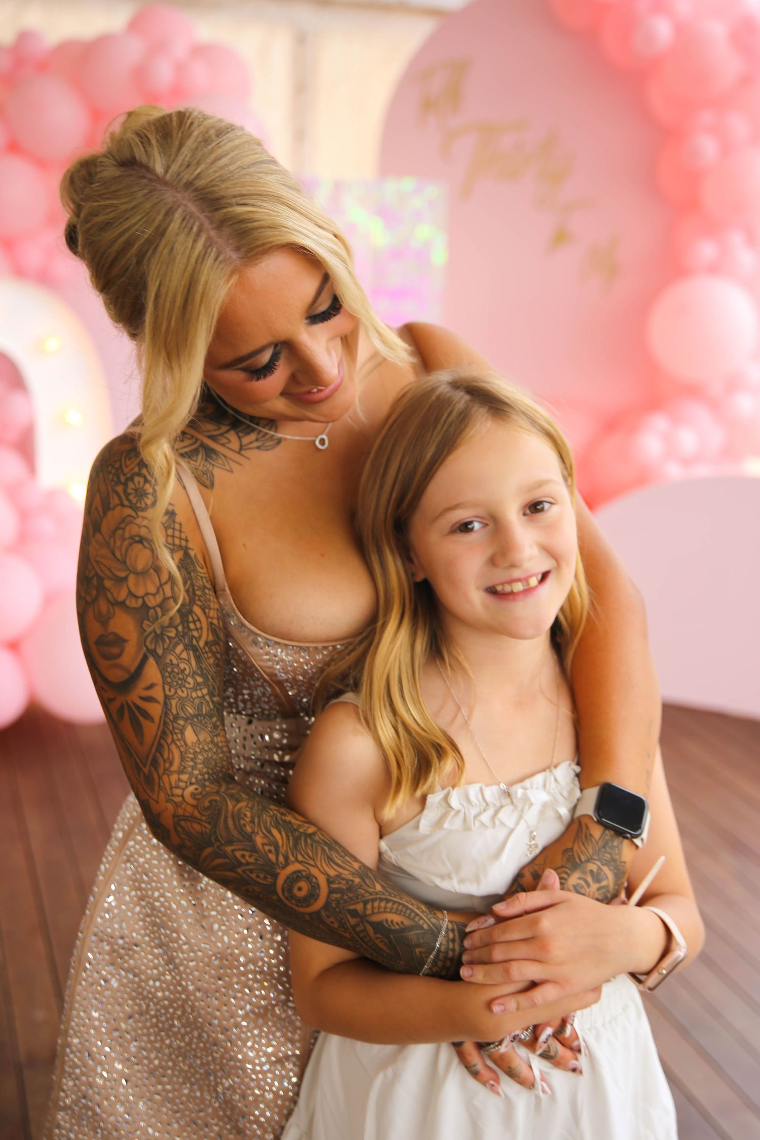 Sweet candid moments captured between two people in sparkly and white dresses with pink balloon backdrop.