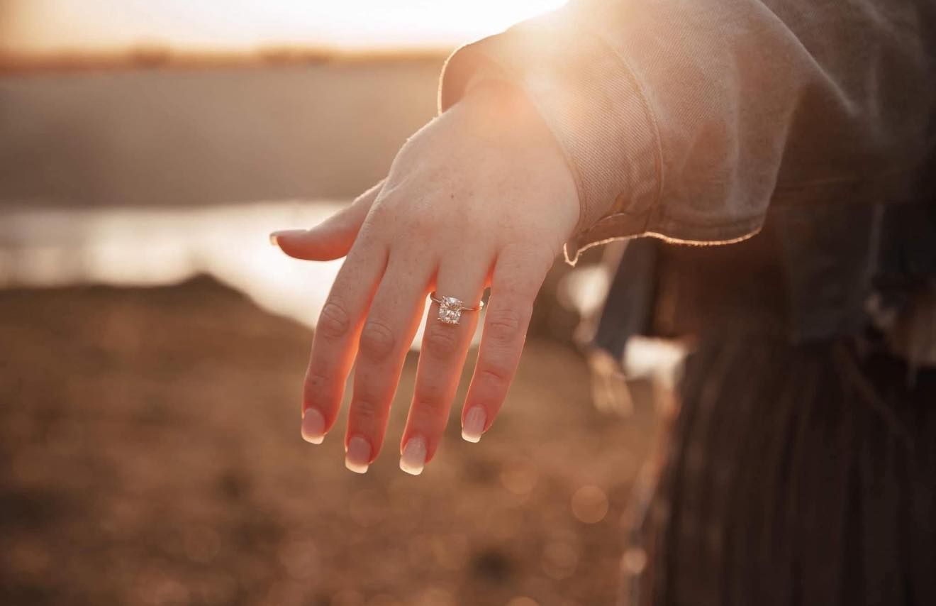 Close-up of hands with wedding rings in golden sunlight.