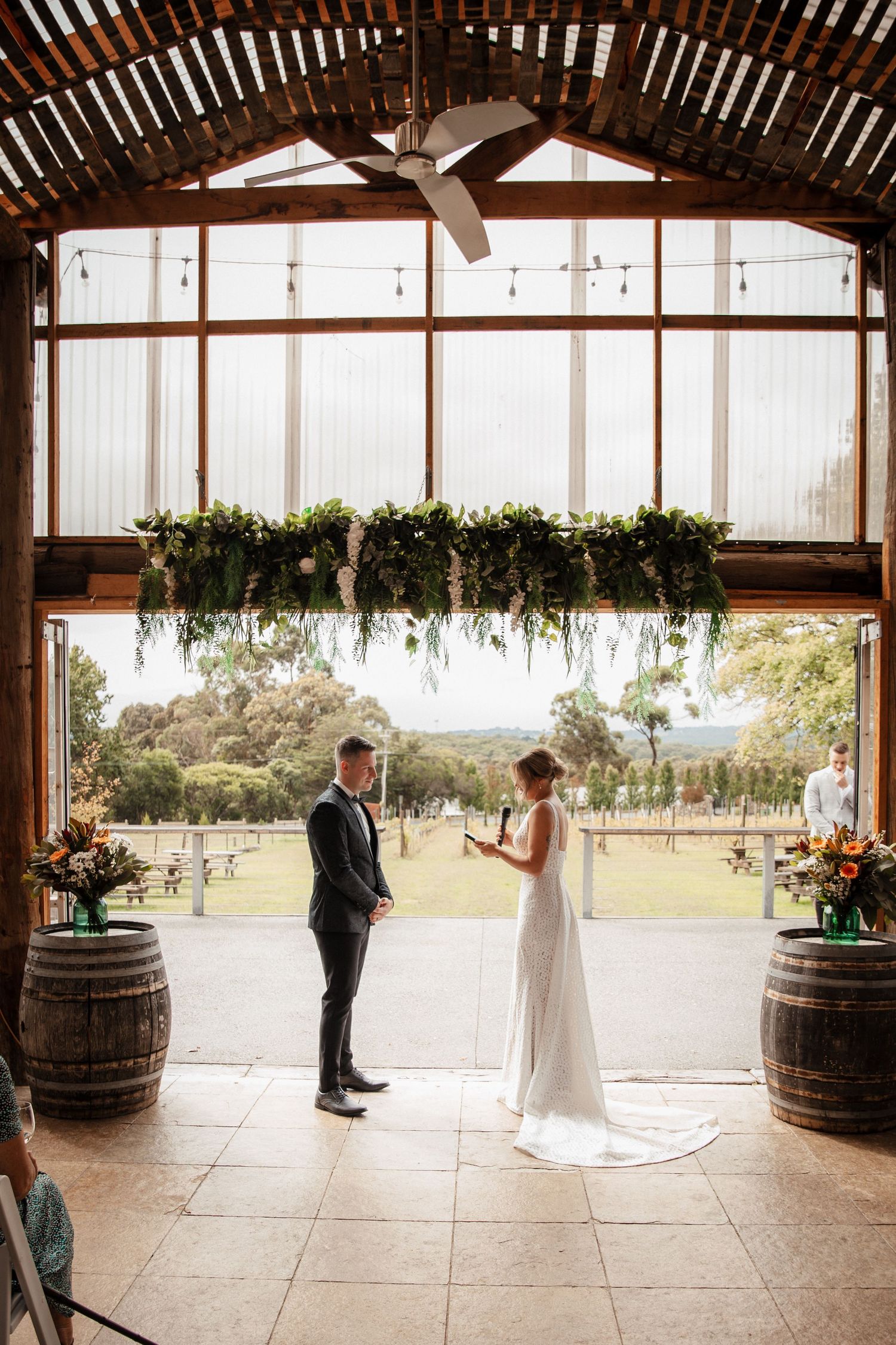 A wedding ceremony takes place in a rustic barn venue with wooden beams and natural lighting. Wedding photography