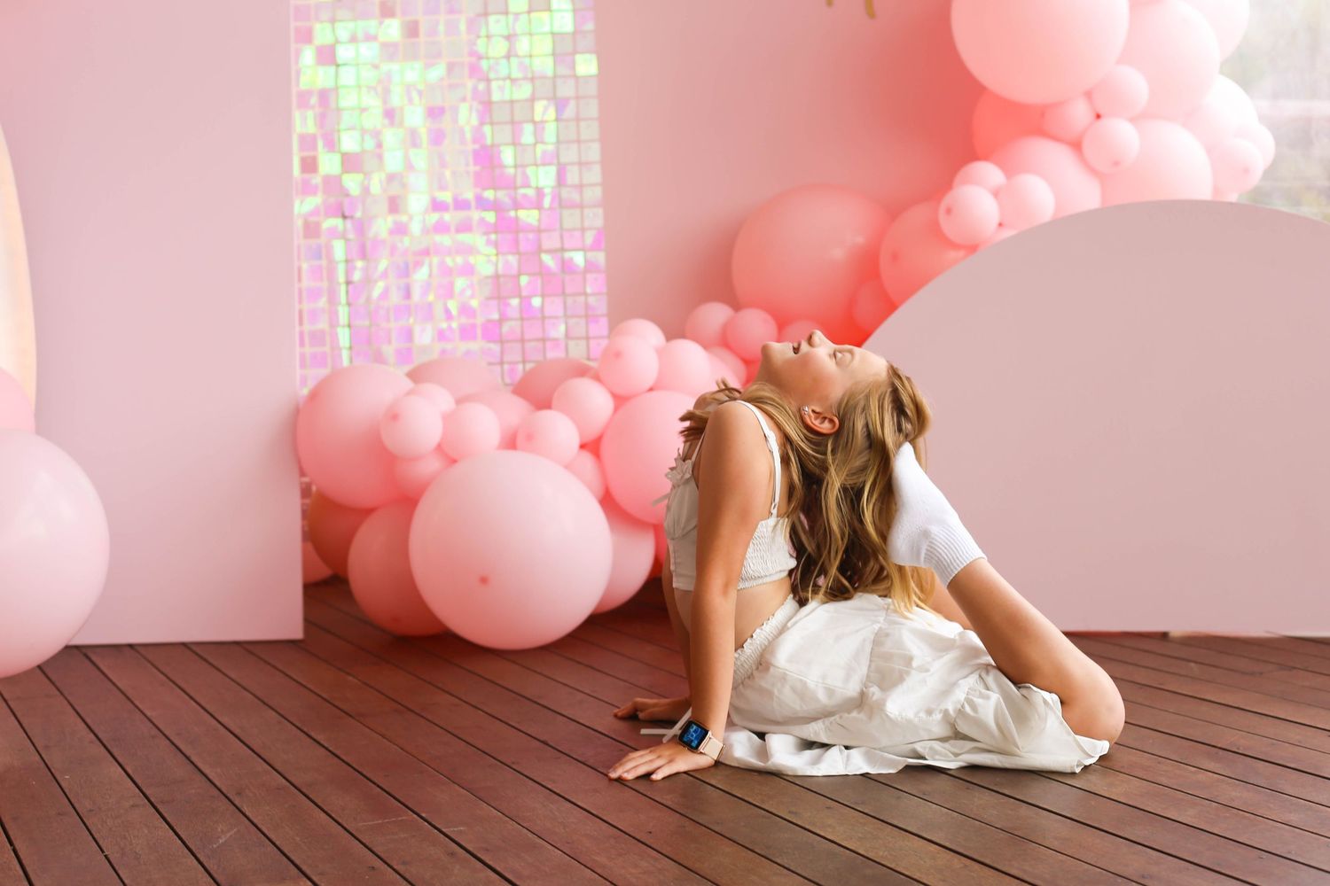 Playful dance moves captured on a wooden floor with pink balloon decorations.