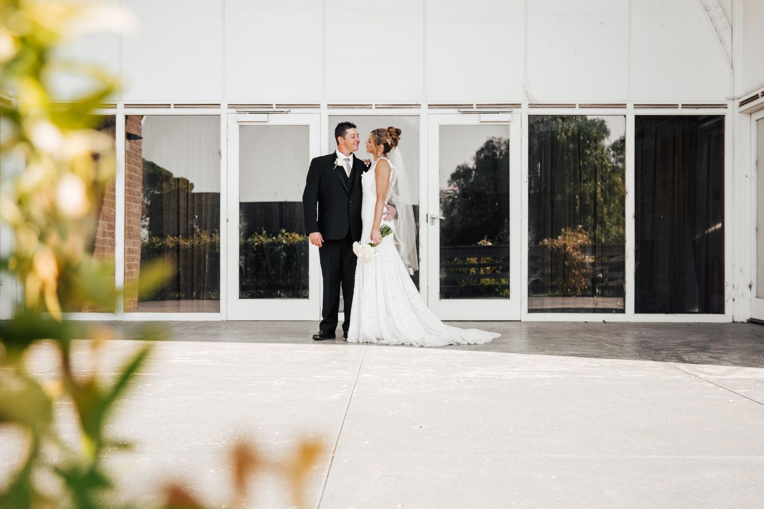Modern white building facade with large windows serves as elegant wedding venue backdrop. Wedding photography