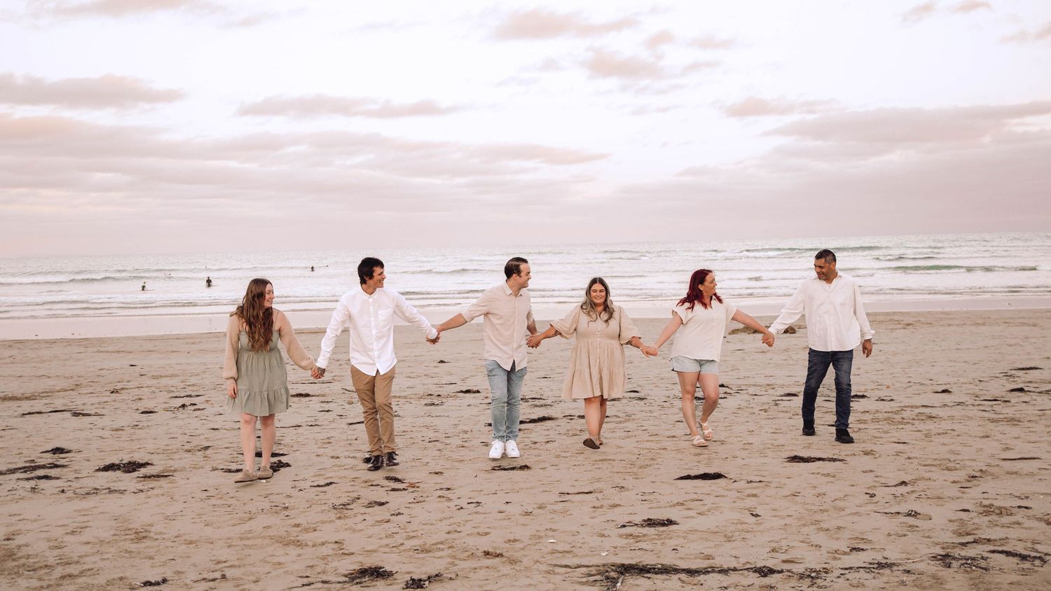 Family members walking hand in hand along beach shoreline at sunset.
