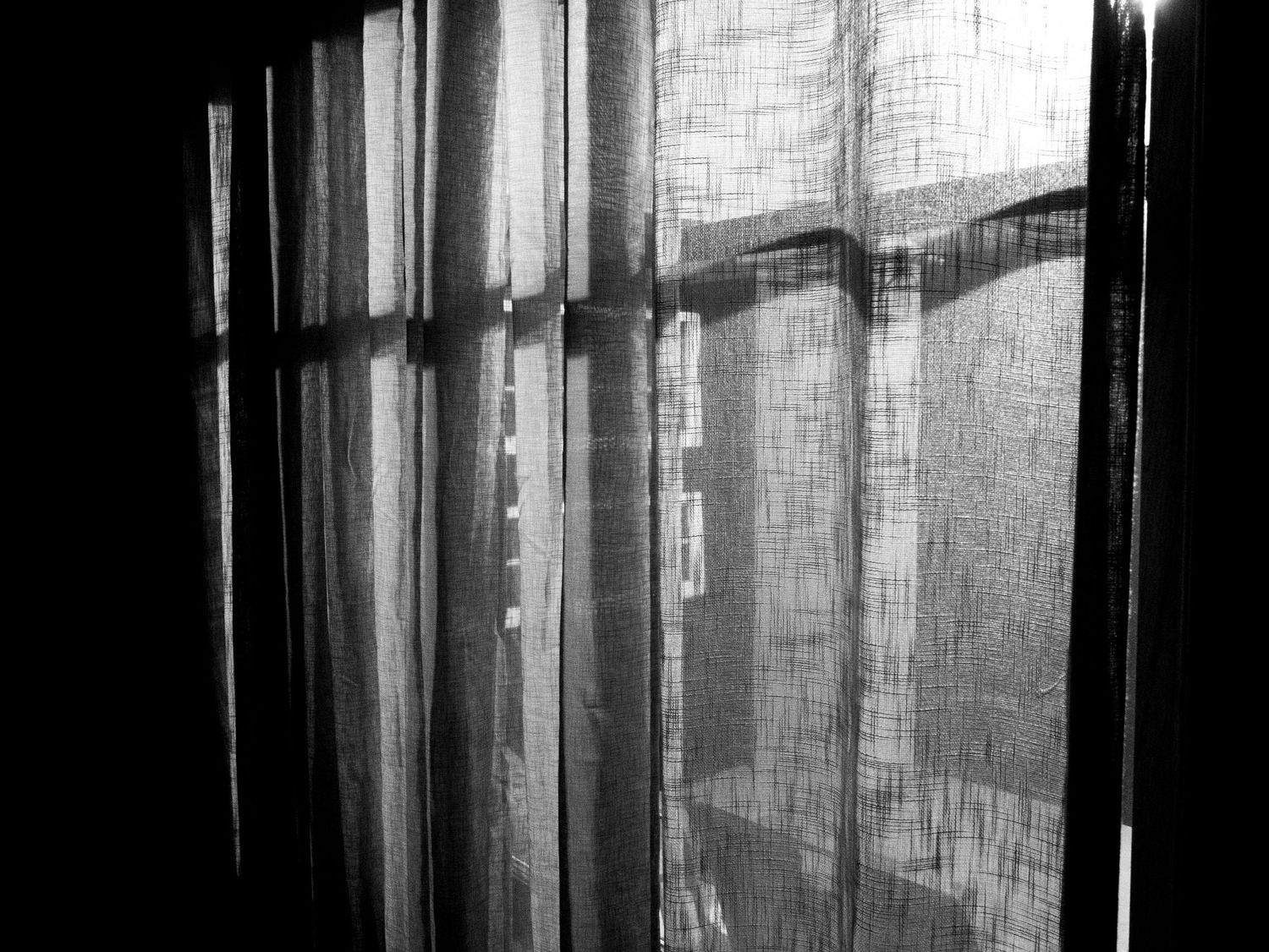 Sunlight filters through sheer curtains creating dramatic shadows and streaks of light in a moody interior space.