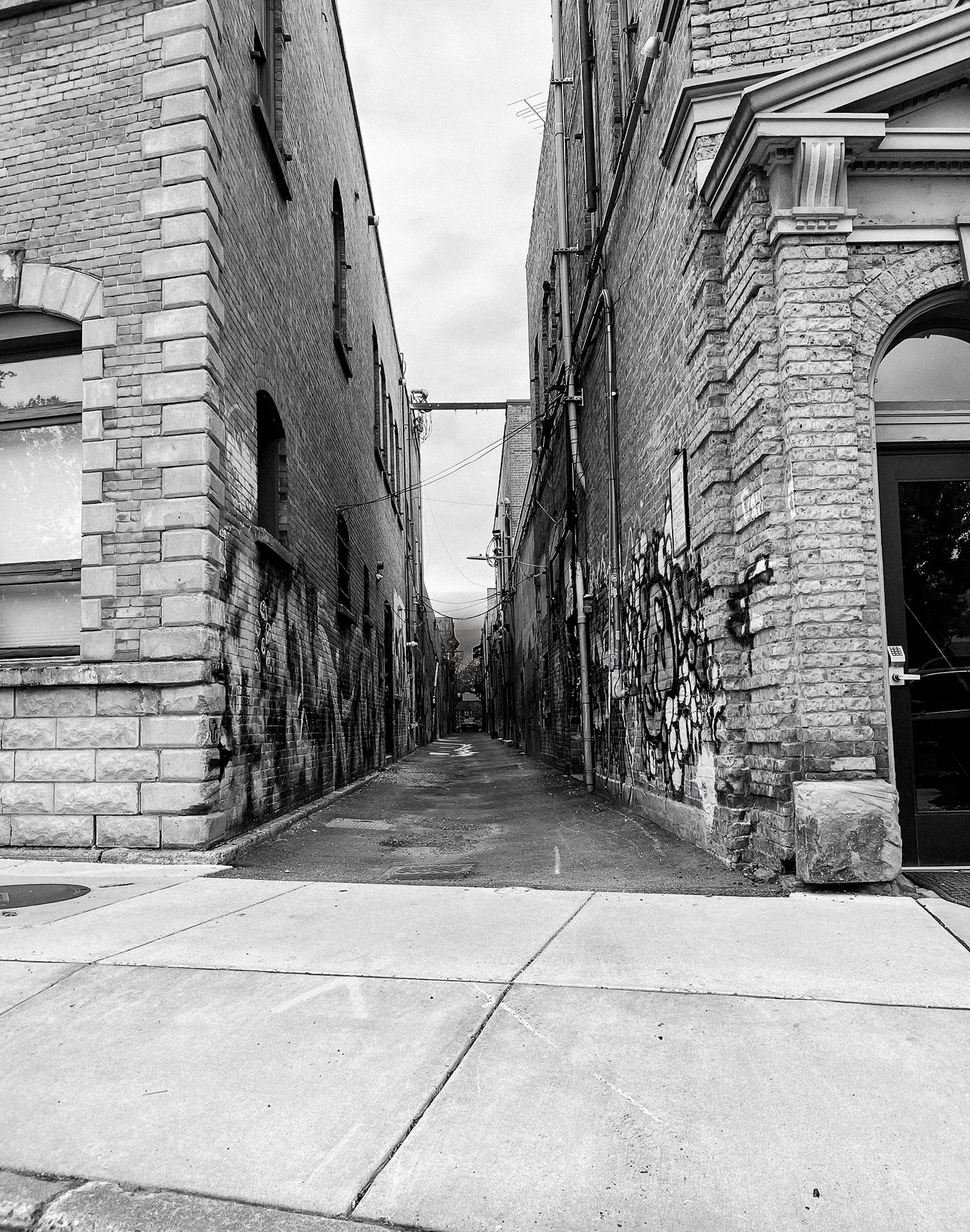 A narrow urban alley with graffiti-covered walls and stone architecture shown from different angles in black and white.
