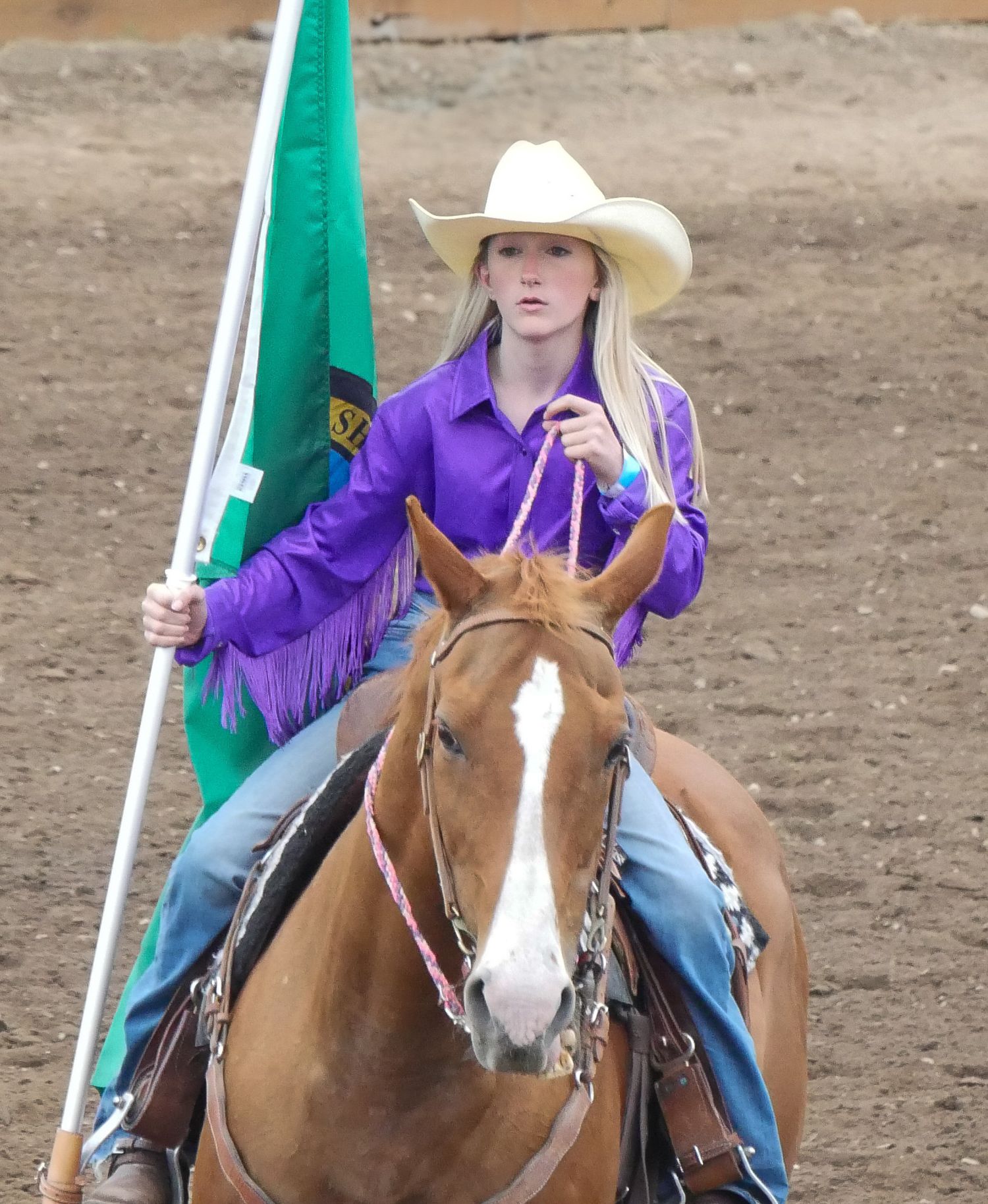 My Daughter in purple attire carrying Washington state flag while riding her horse in a dirt arena.