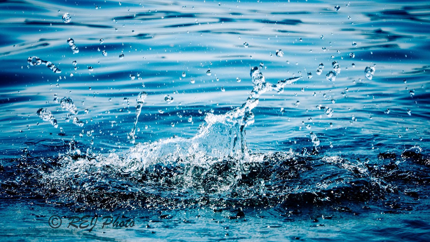 Water splashing and creating dynamic droplets against a blue rippled ocean surface in bright sunlight.