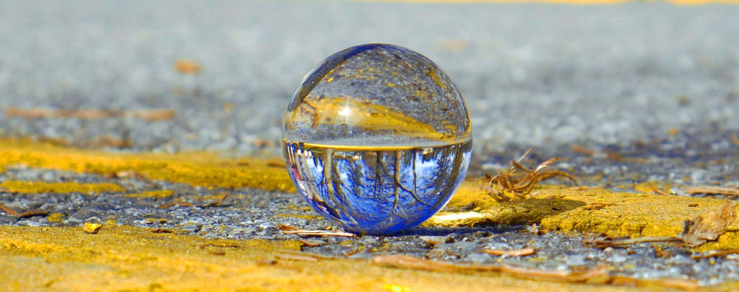 A crystal ball resting on a yellow-painted curb, reflecting blue sky and trees in its transparent sphere.