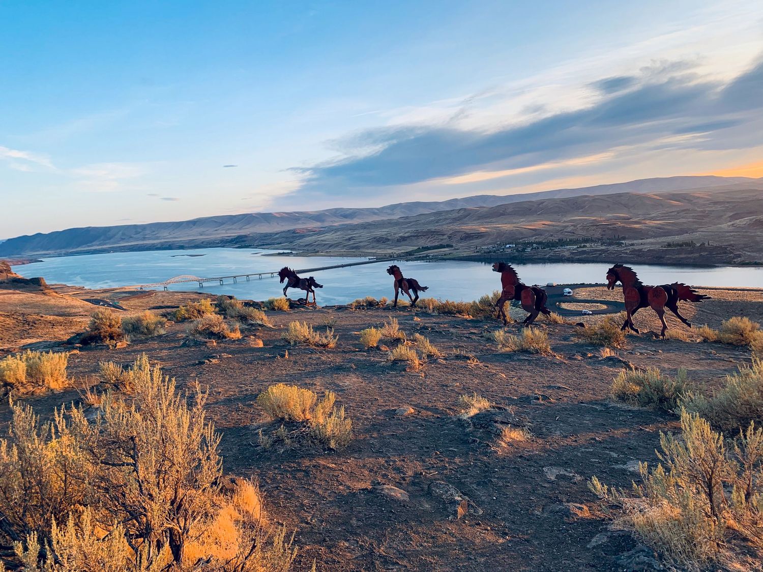 Wild horses Monument along a scenic Columbia river basin ridge at sunset with golden light illuminating the desert landscape.