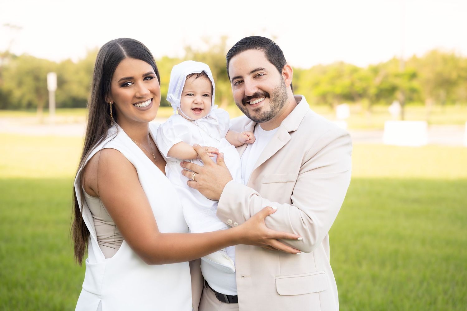 Family wearing white outfits poses together outdoors in a grassy field during golden hour.