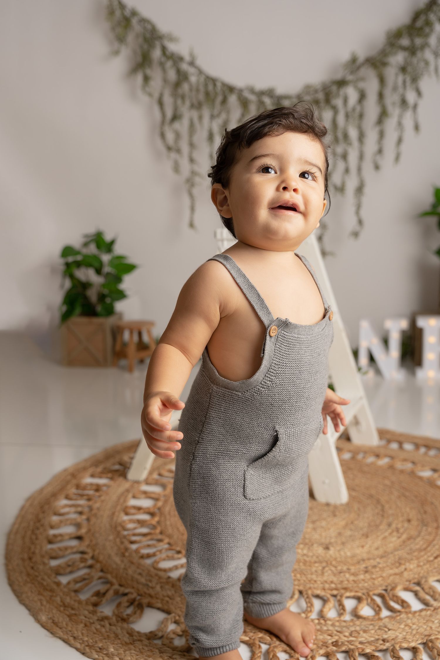 Baby wearing grey outfit explores while crawling on circular natural fiber mat with tassels.