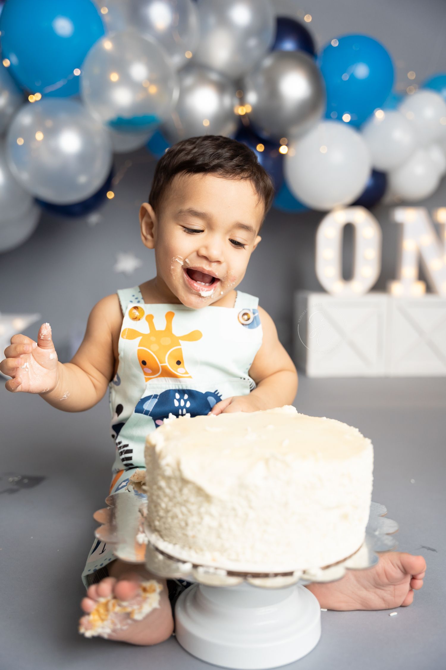 White birthday cake smash session with blue and silver balloon decorations.