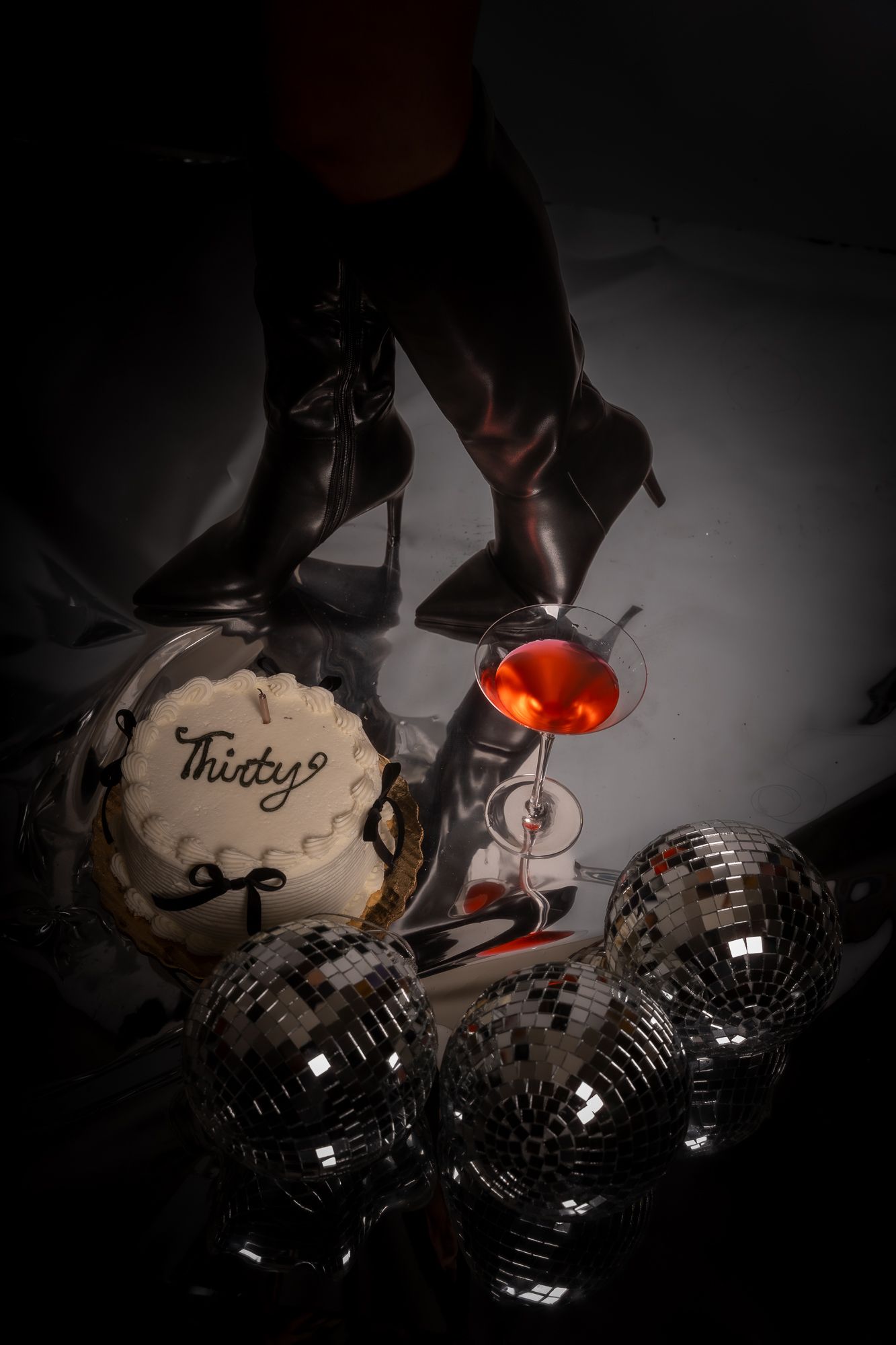 Dramatic low-light photo of birthday cake and disco balls with red cocktail glow.