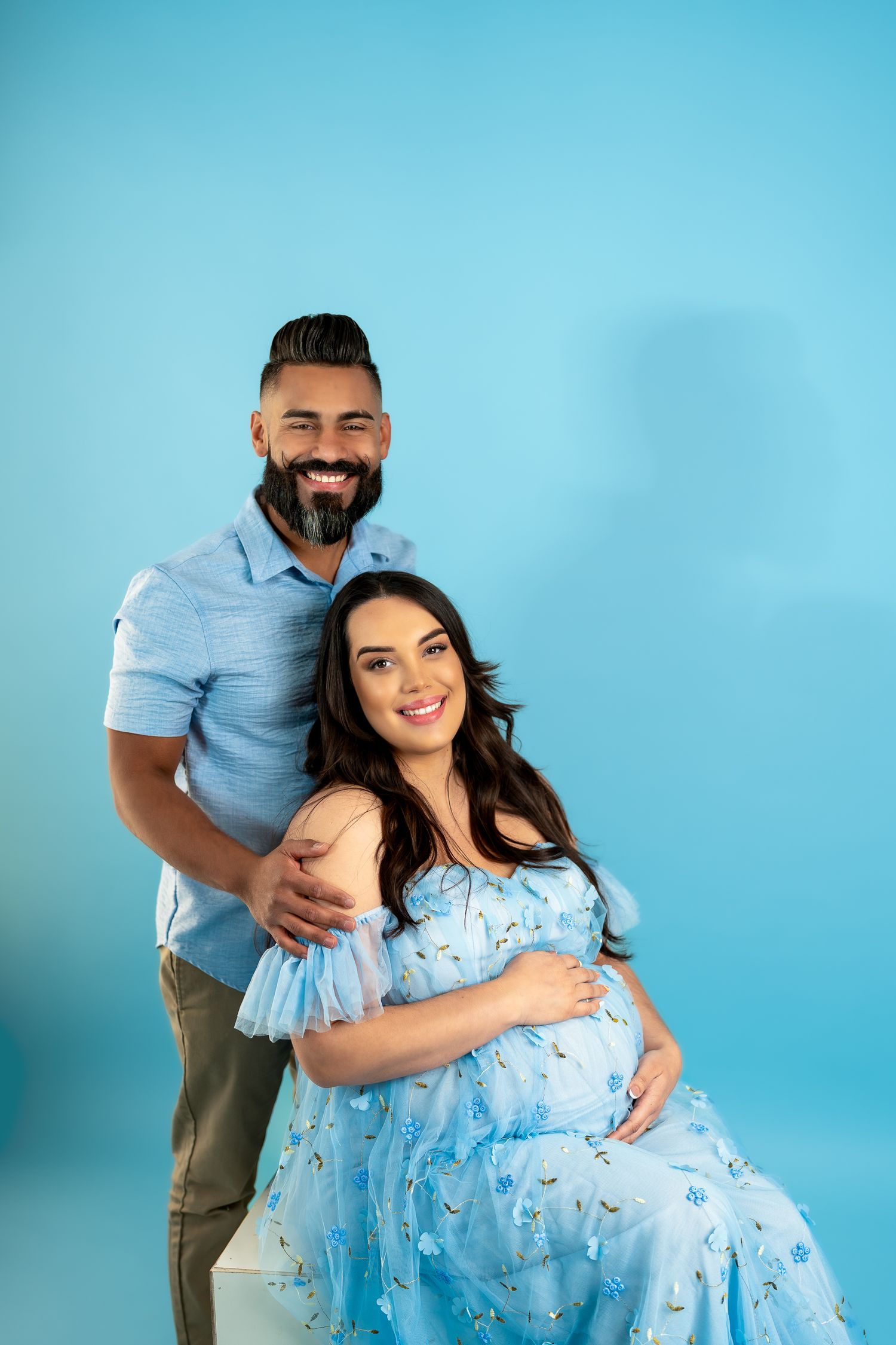 Romantic couple embraces while wearing coordinated blue attire in studio photoshoot.
