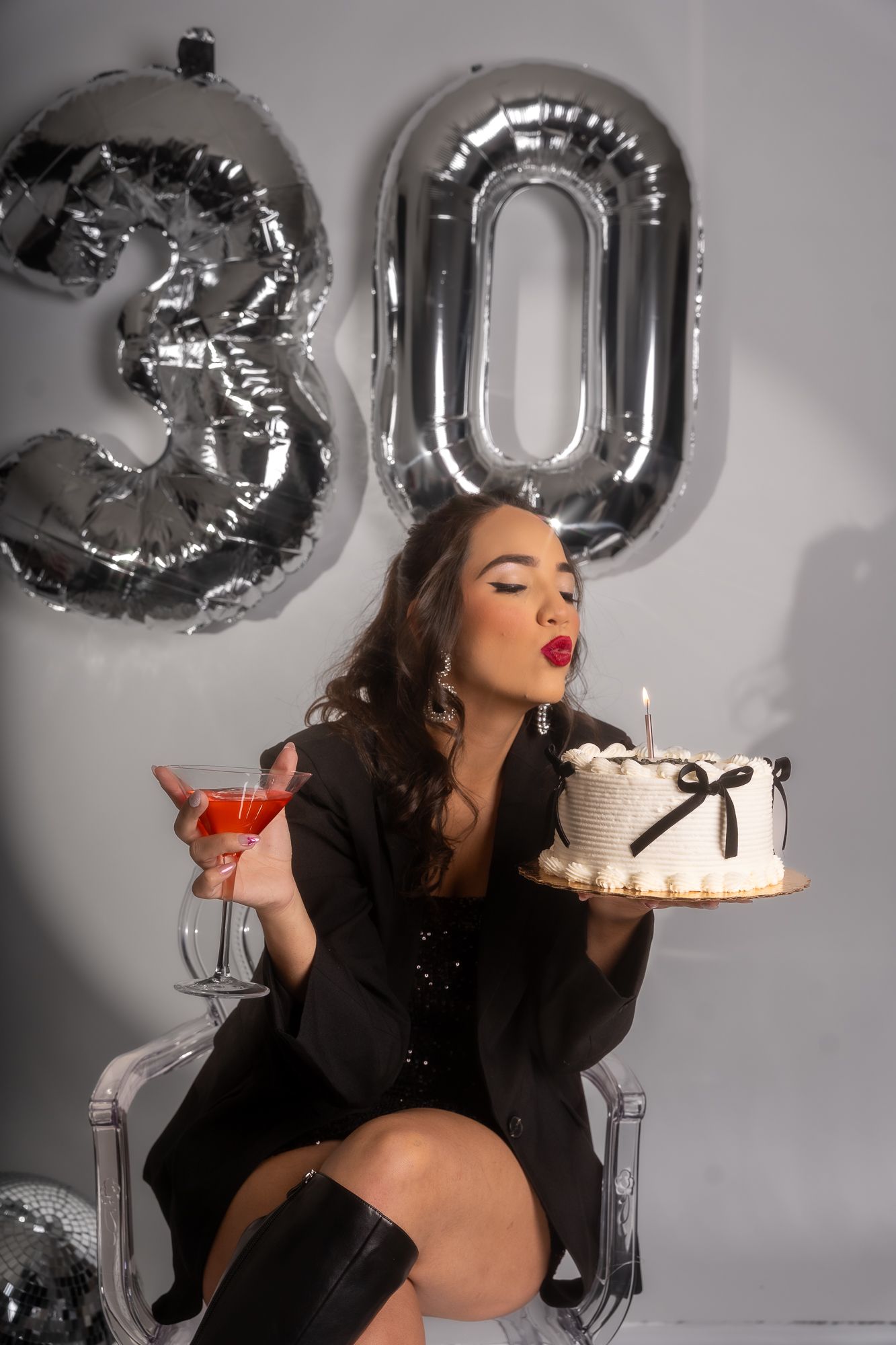 Celebratory birthday scene with silver '30' balloons, red martini and white cake with black bow.