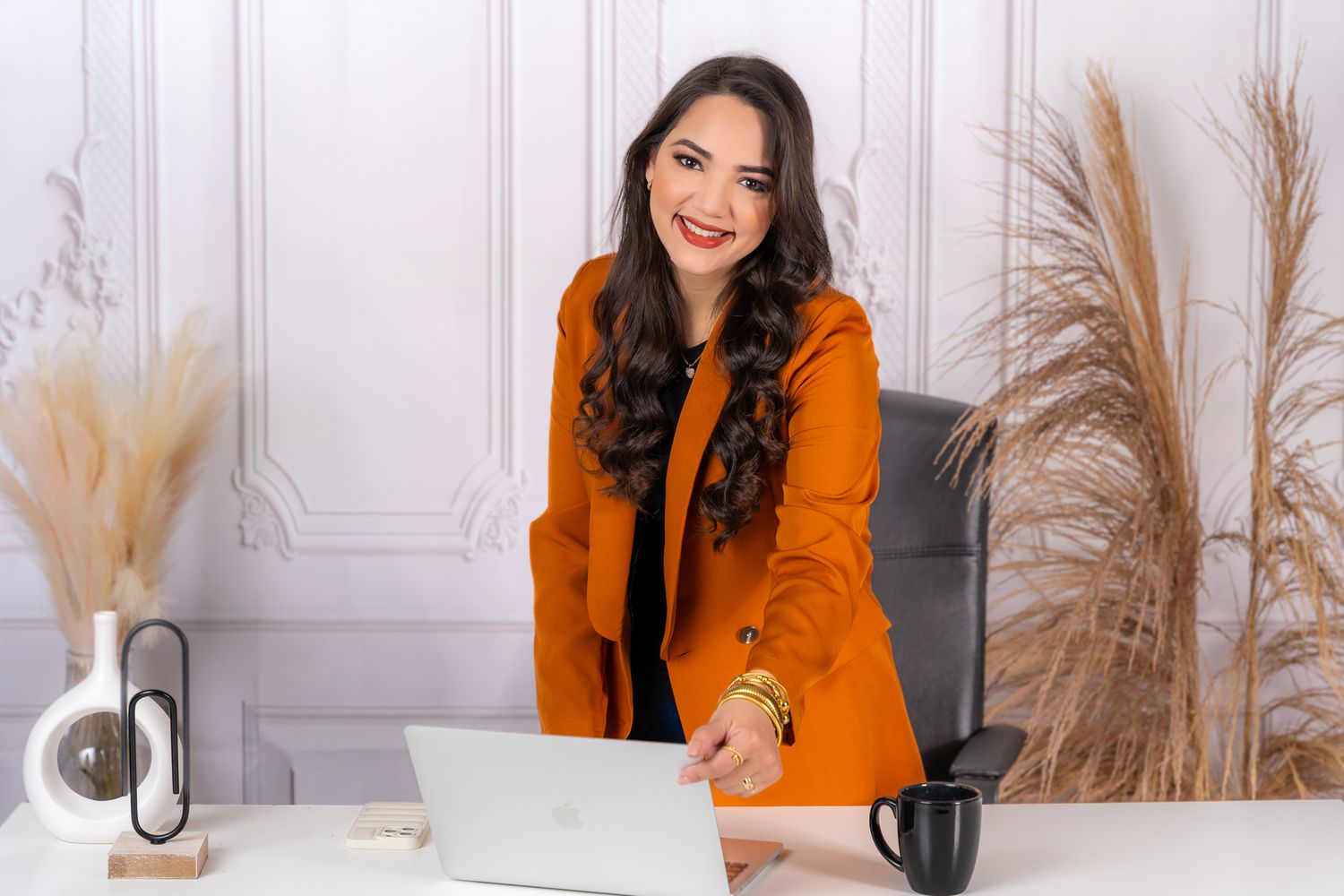 Professional workspace setup with laptop, pampas grass decor, and person in orange blazer.