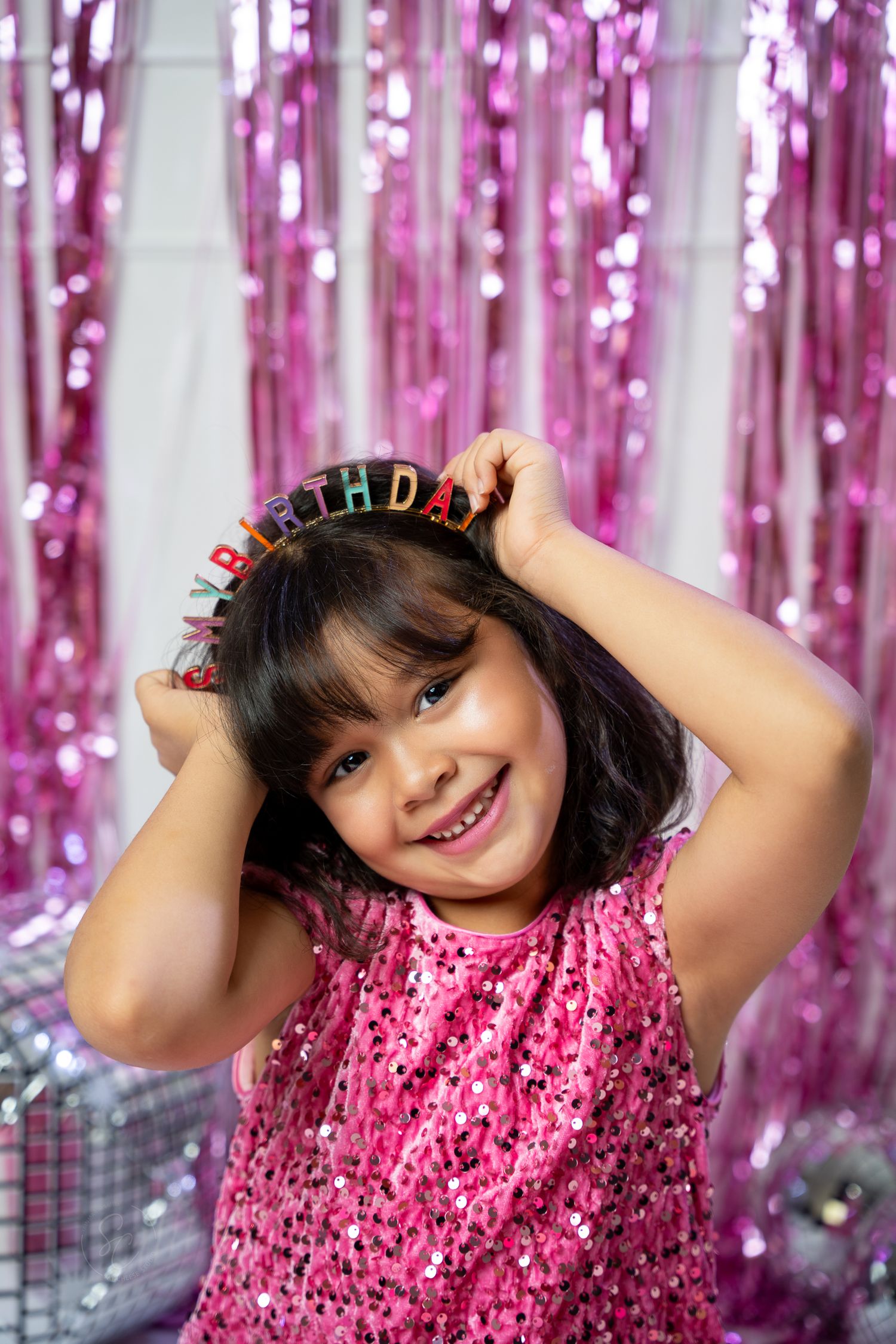 Pink sequined outfit shimmers against metallic fringe backdrop in festive photo setting.