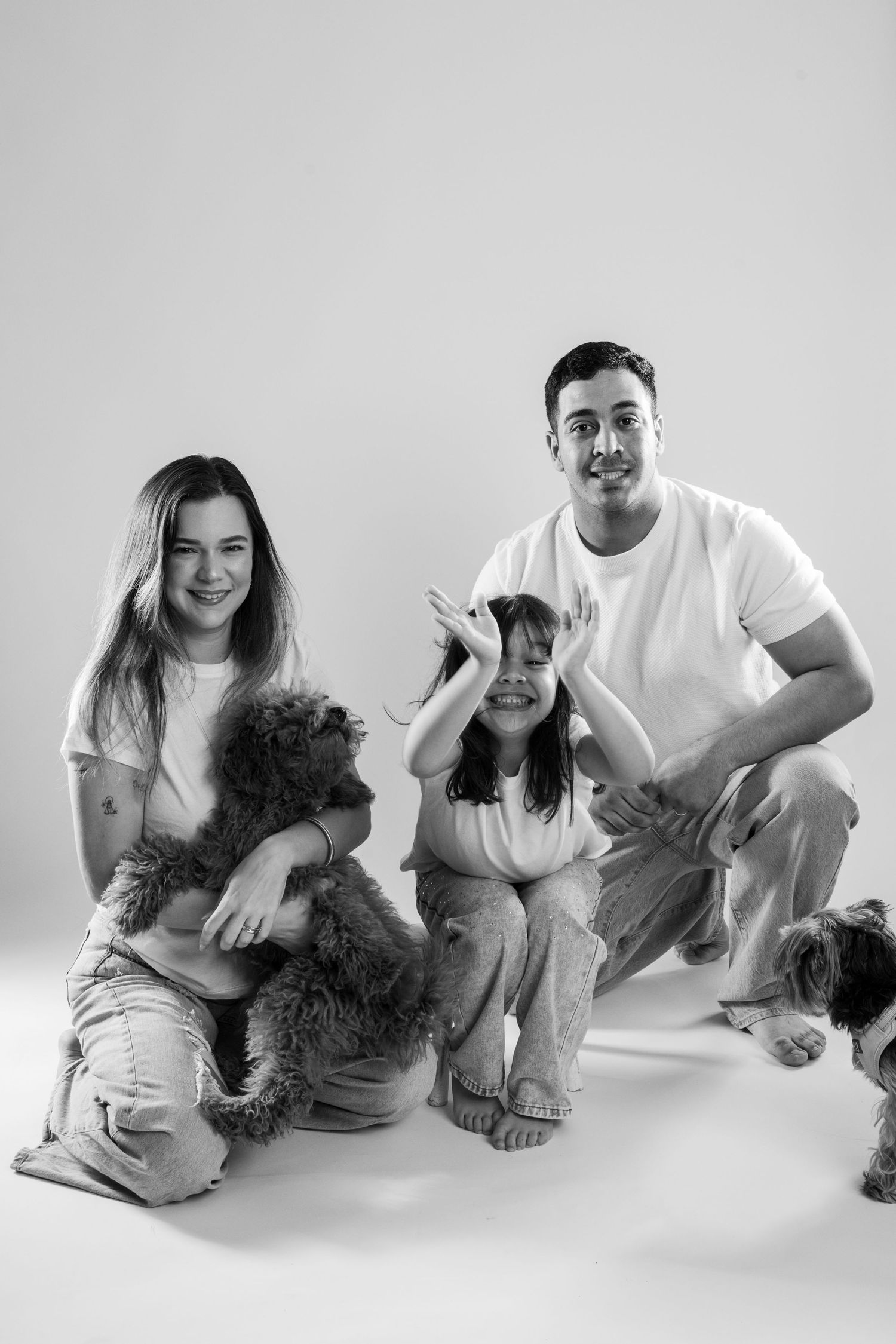 Family photo session with playful poses and a small dog against white background.