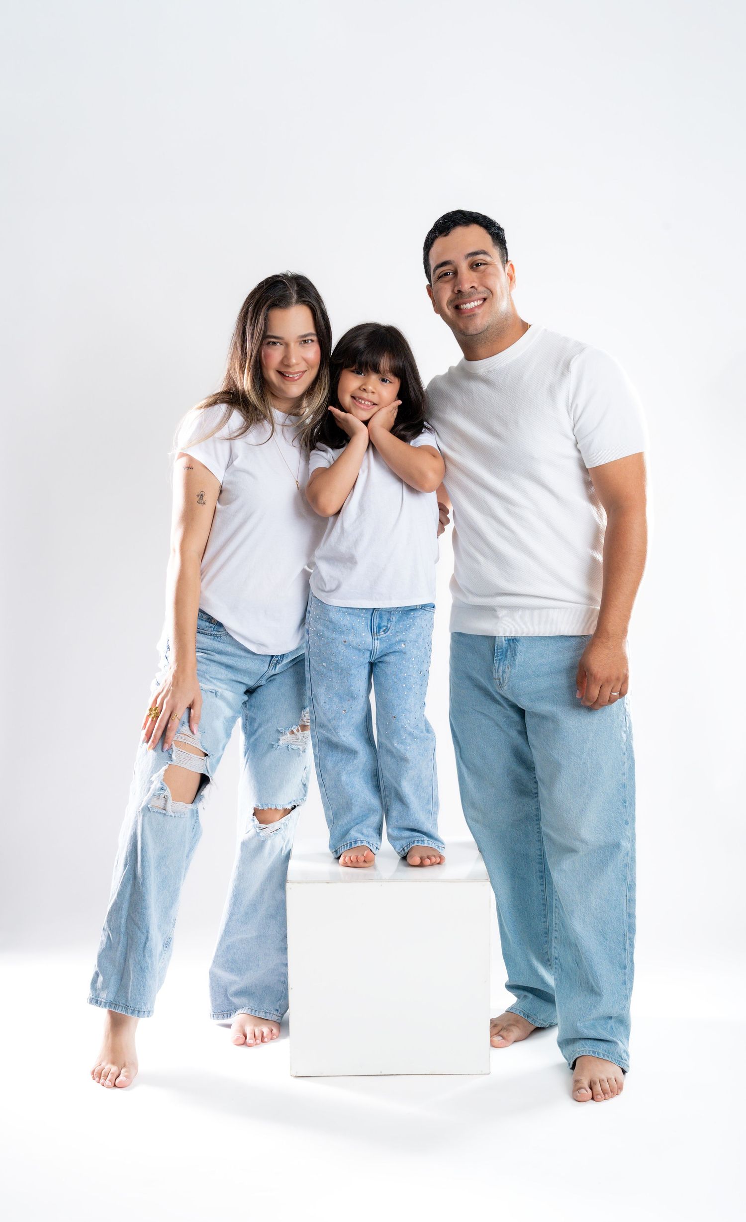 Family wearing matching denim and white outfits pose together against white background.