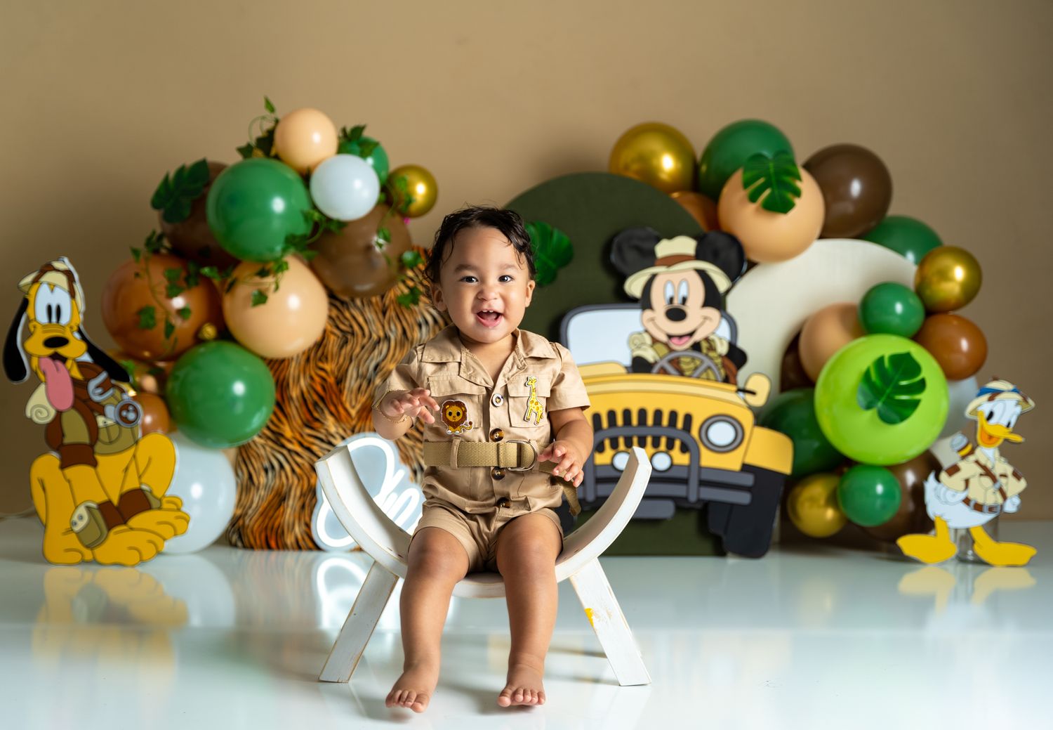 Safari themed first birthday setup with animal prints and green balloon garland.