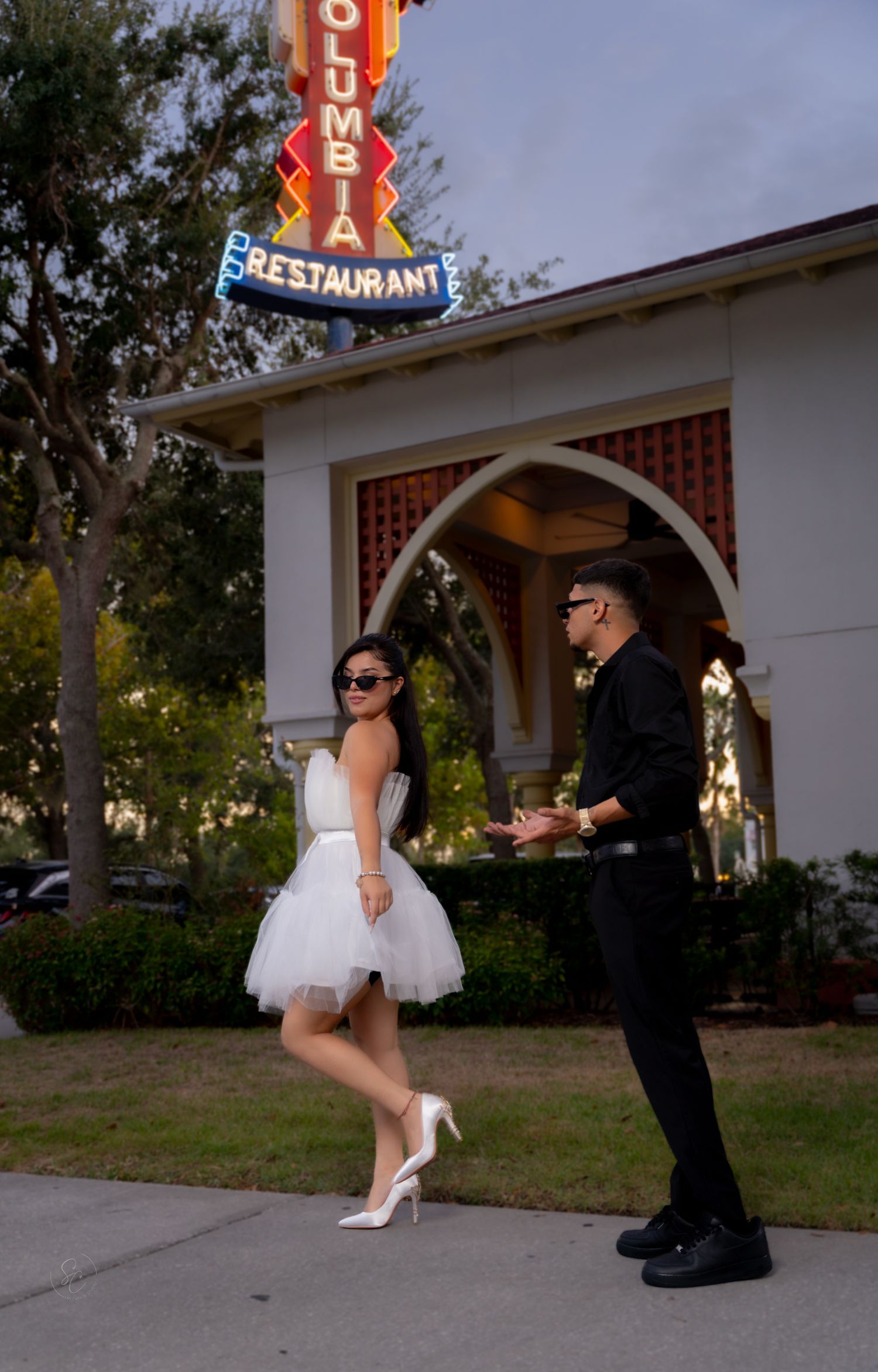 Couple poses playfully outside a retro restaurant with vintage neon signage.