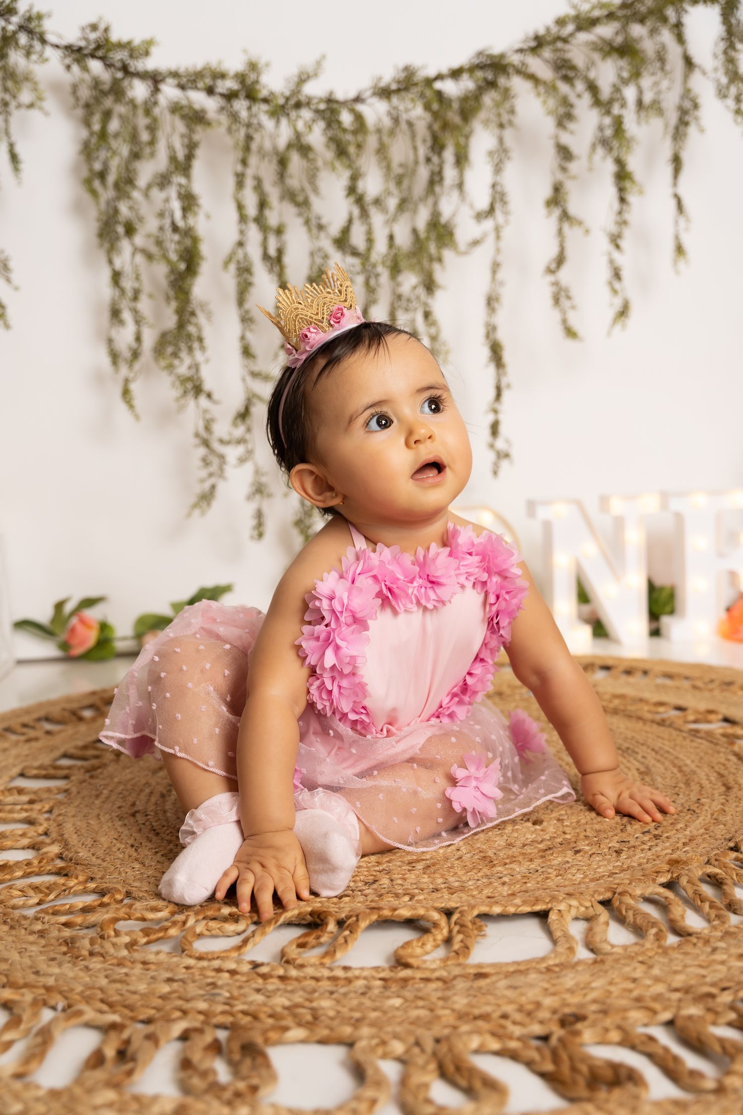 Natural light birthday session with rustic woven mat and delicate hanging foliage.