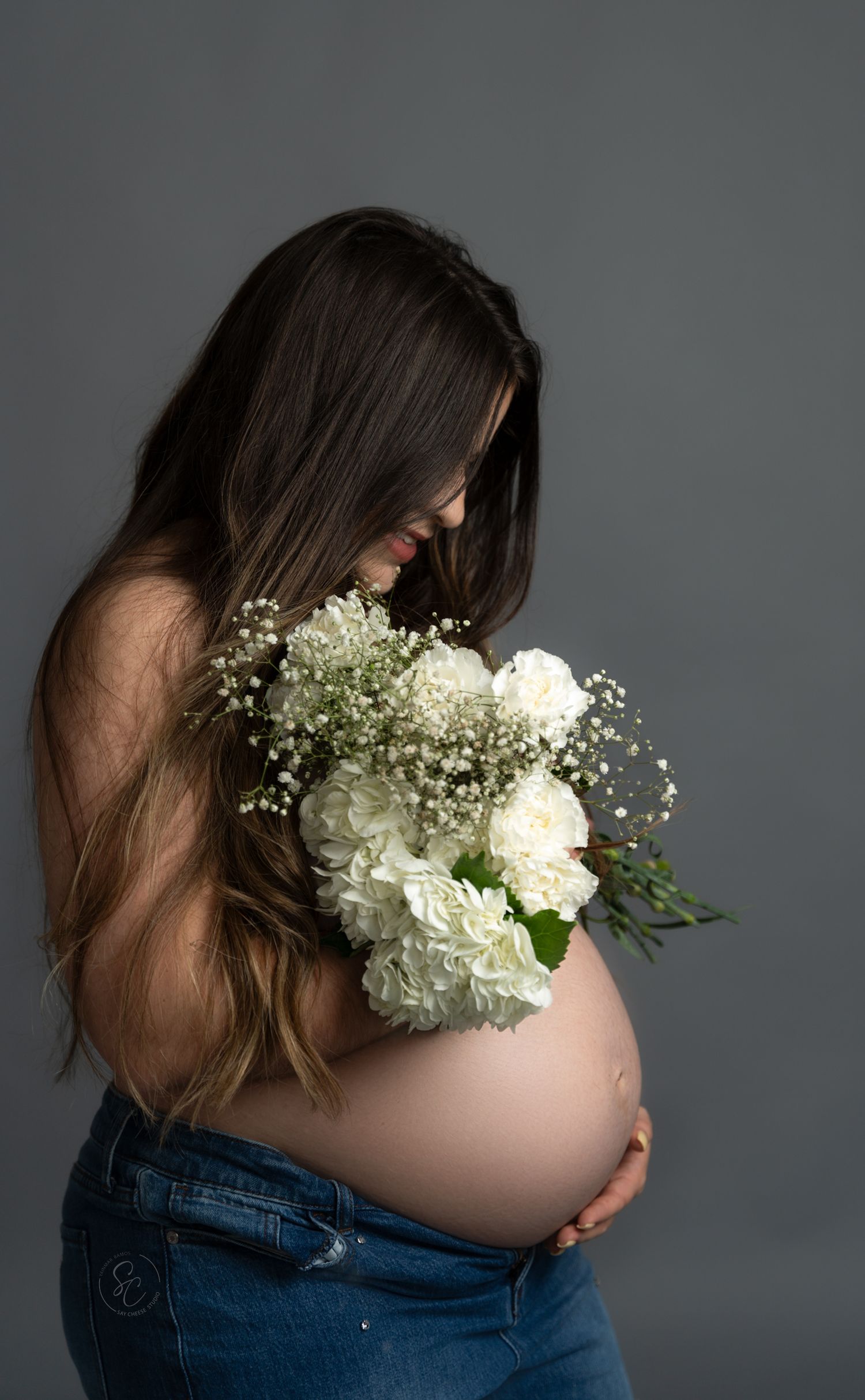 Artistic maternity photo with white flowers and baby's breath against pregnant belly in denim.