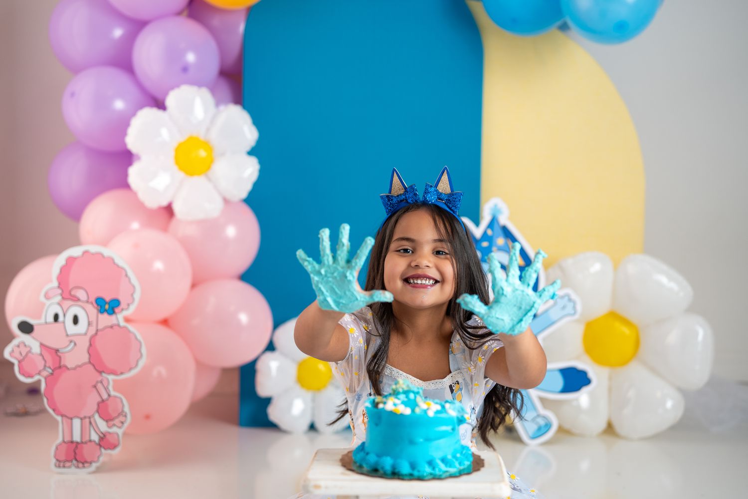 Festive birthday backdrop with pink, blue, and yellow balloons and floral accents.