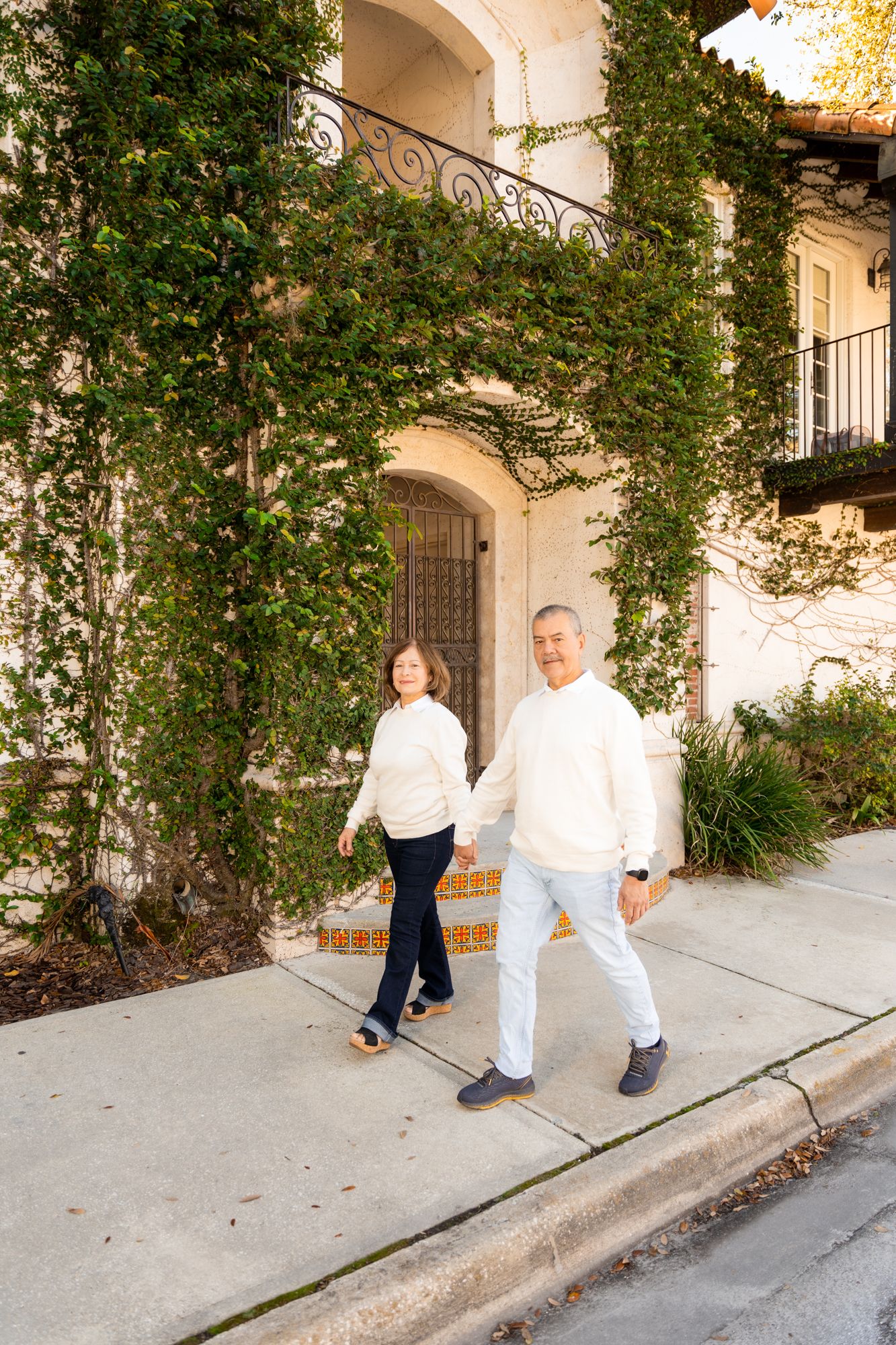 Family in white outfits poses playfully along Spanish colonial architecture with climbing vines.