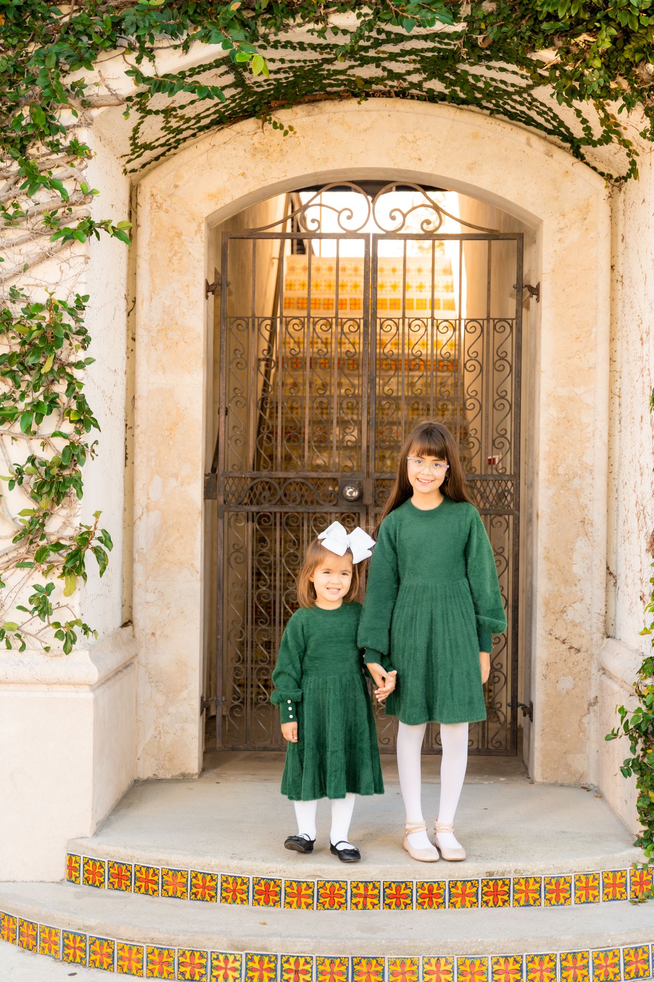 Mother and children in matching green outfits pose in Spanish-style archway.