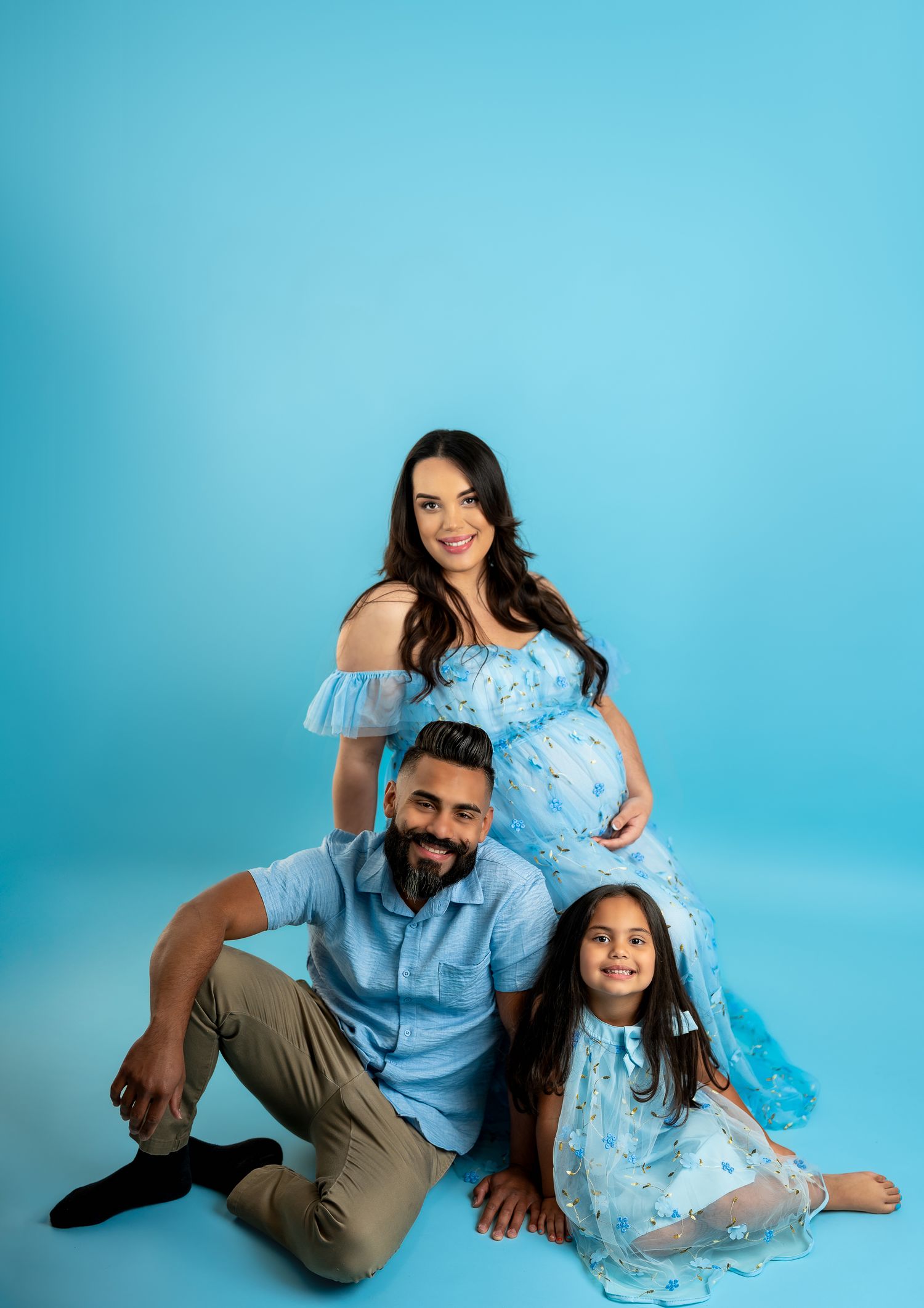 Family poses playfully on floor against bright blue backdrop in coordinated outfits.