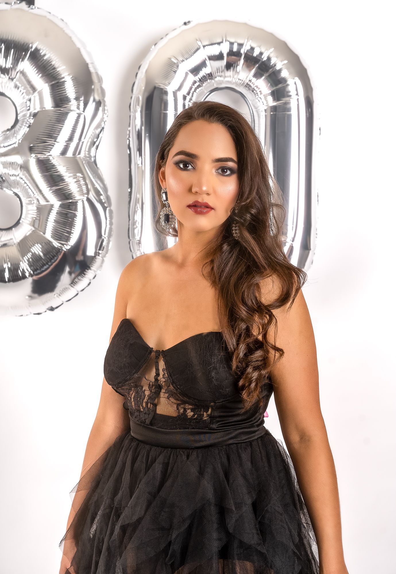 Elegant portrait in black tulle dress with silver balloon numbers in background.