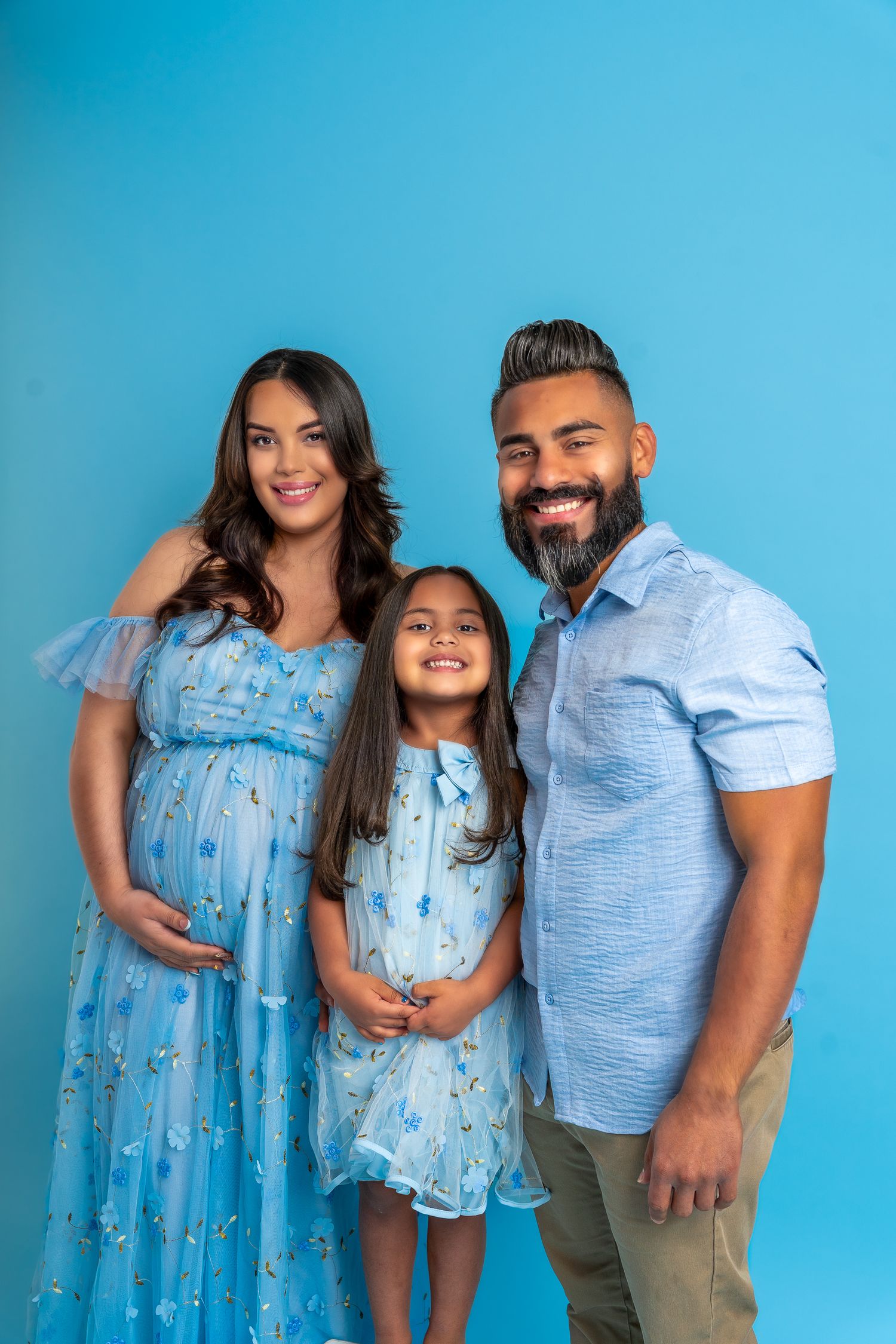 Family wearing coordinated blue outfits poses against bright turquoise background.