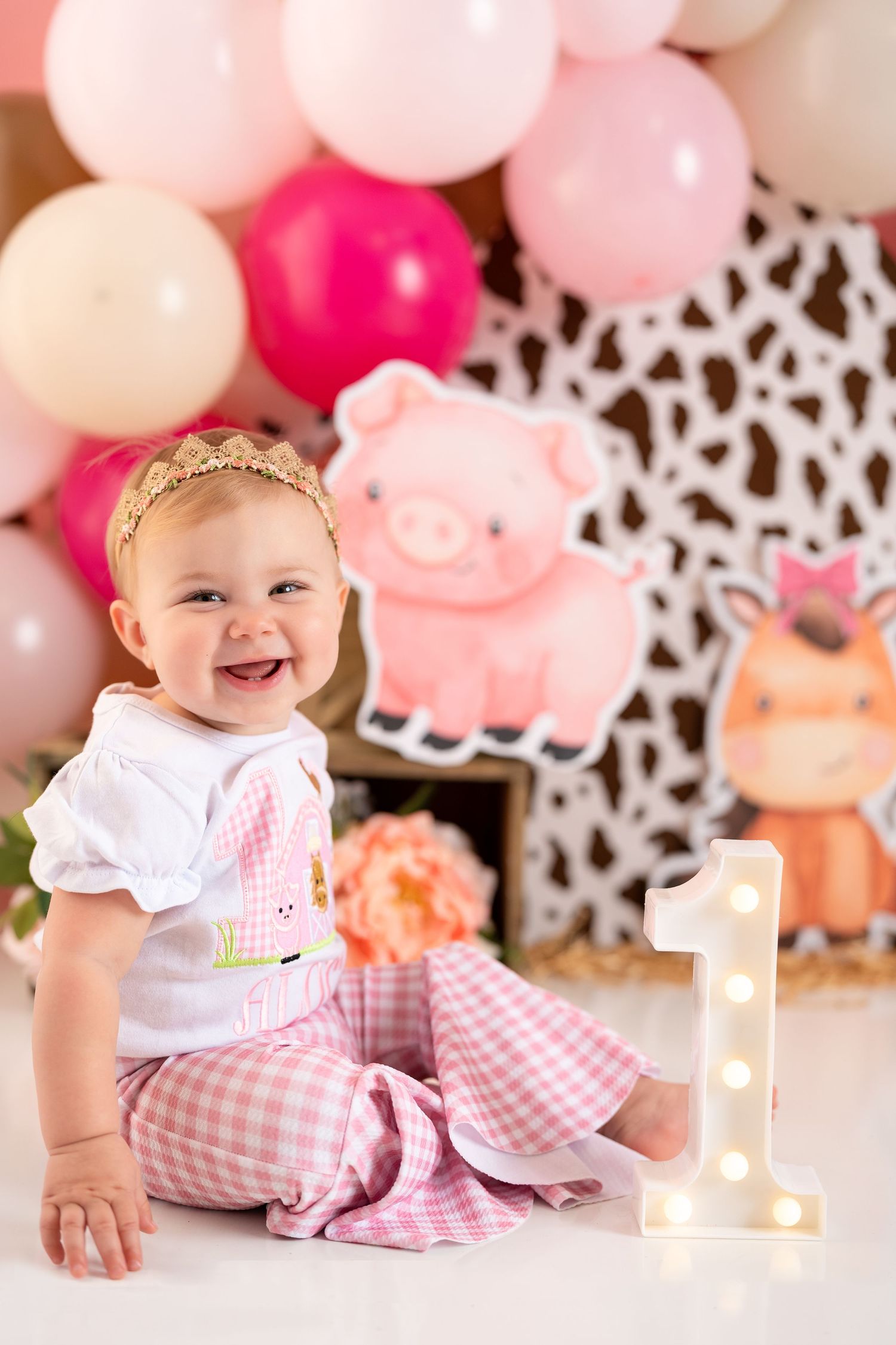 Baby's first birthday setup with pink gingham outfit and cow print backdrop.