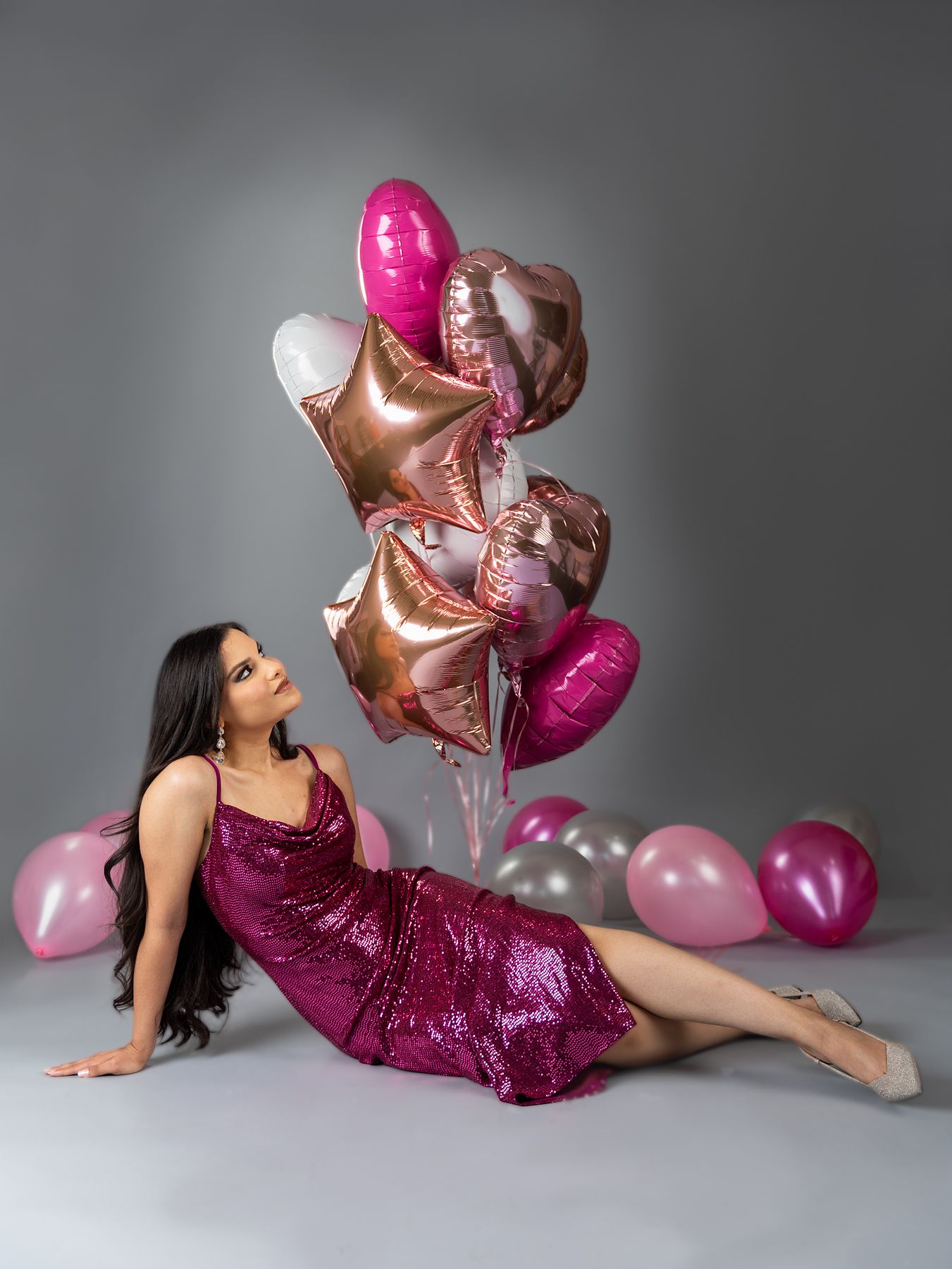 Glamorous pose with metallic balloons and sparkly magenta dress on grey background.