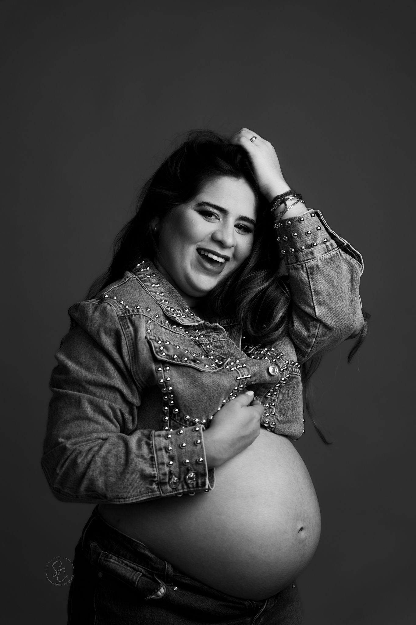 Black and white maternity portrait with embellished denim jacket creating dramatic contrast.