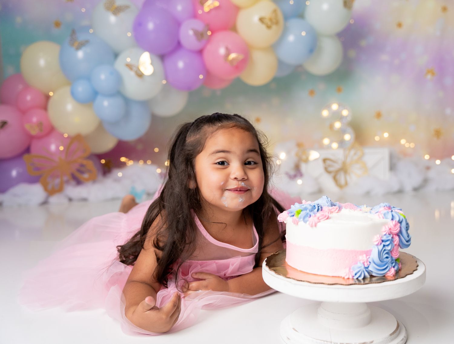 Birthday celebration scene with colorful balloons and white cake on pink backdrop.