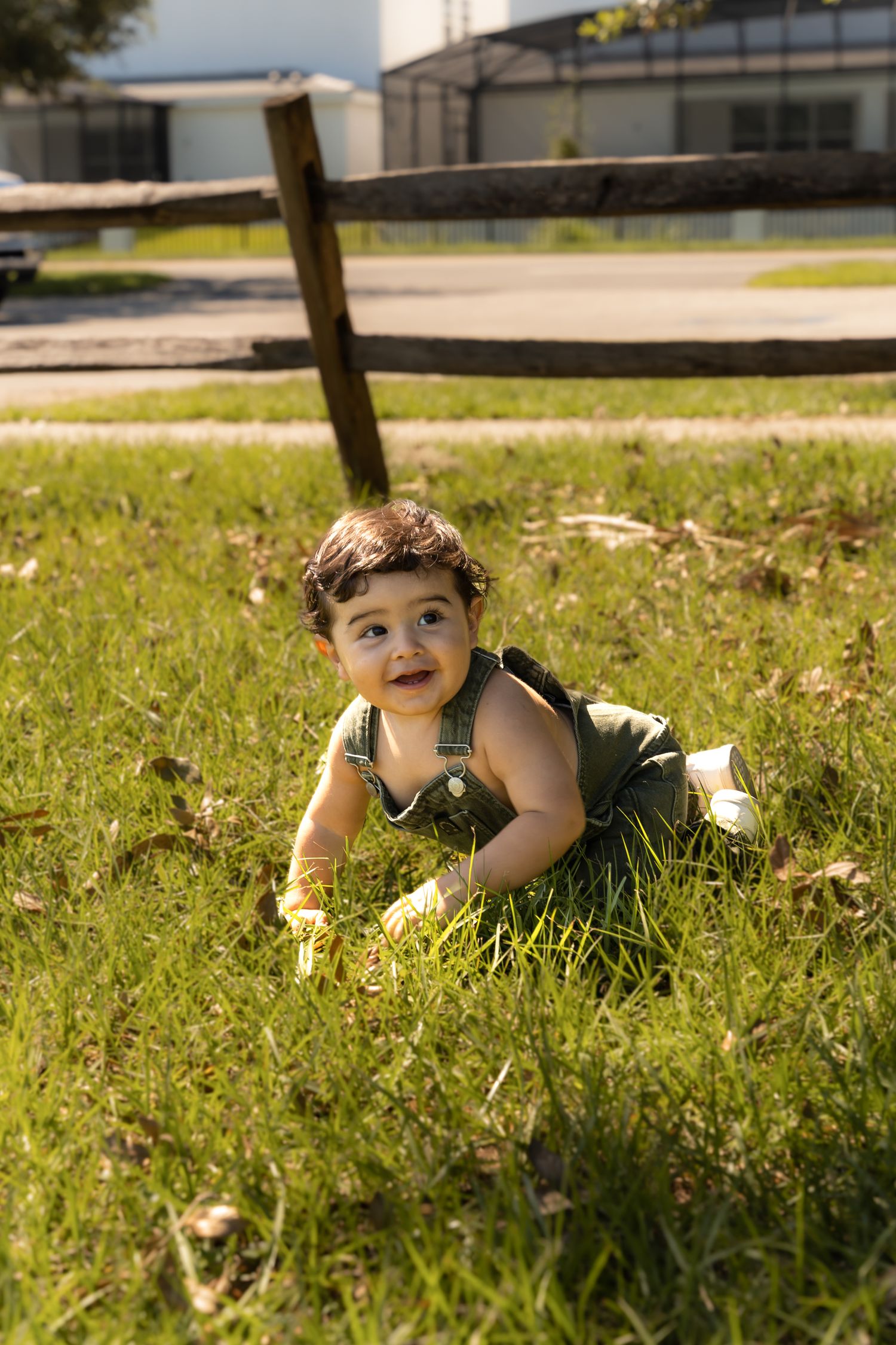 Child relaxing on grassy lawn near wooden fence on bright sunny afternoon.