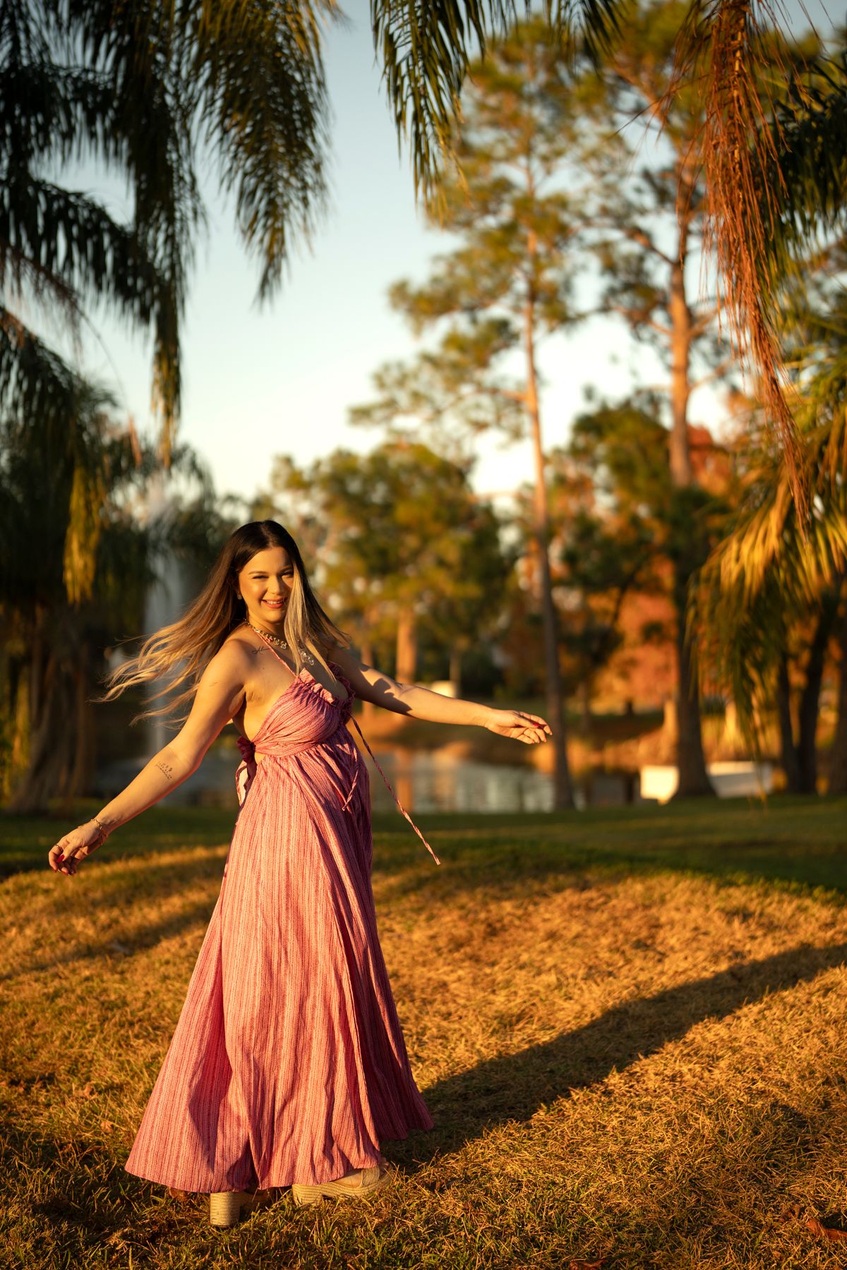 Woman in flowing mauve dress twirling in golden sunset light among palm trees.