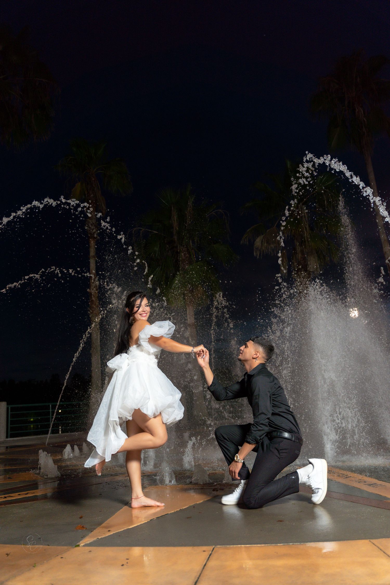 A romantic nighttime dance pose with water fountains spraying in the background.