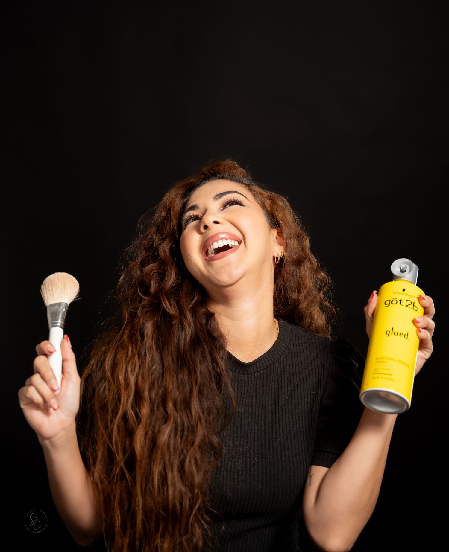 Person in black shirt holds up hair products while posing expressively against dark background.