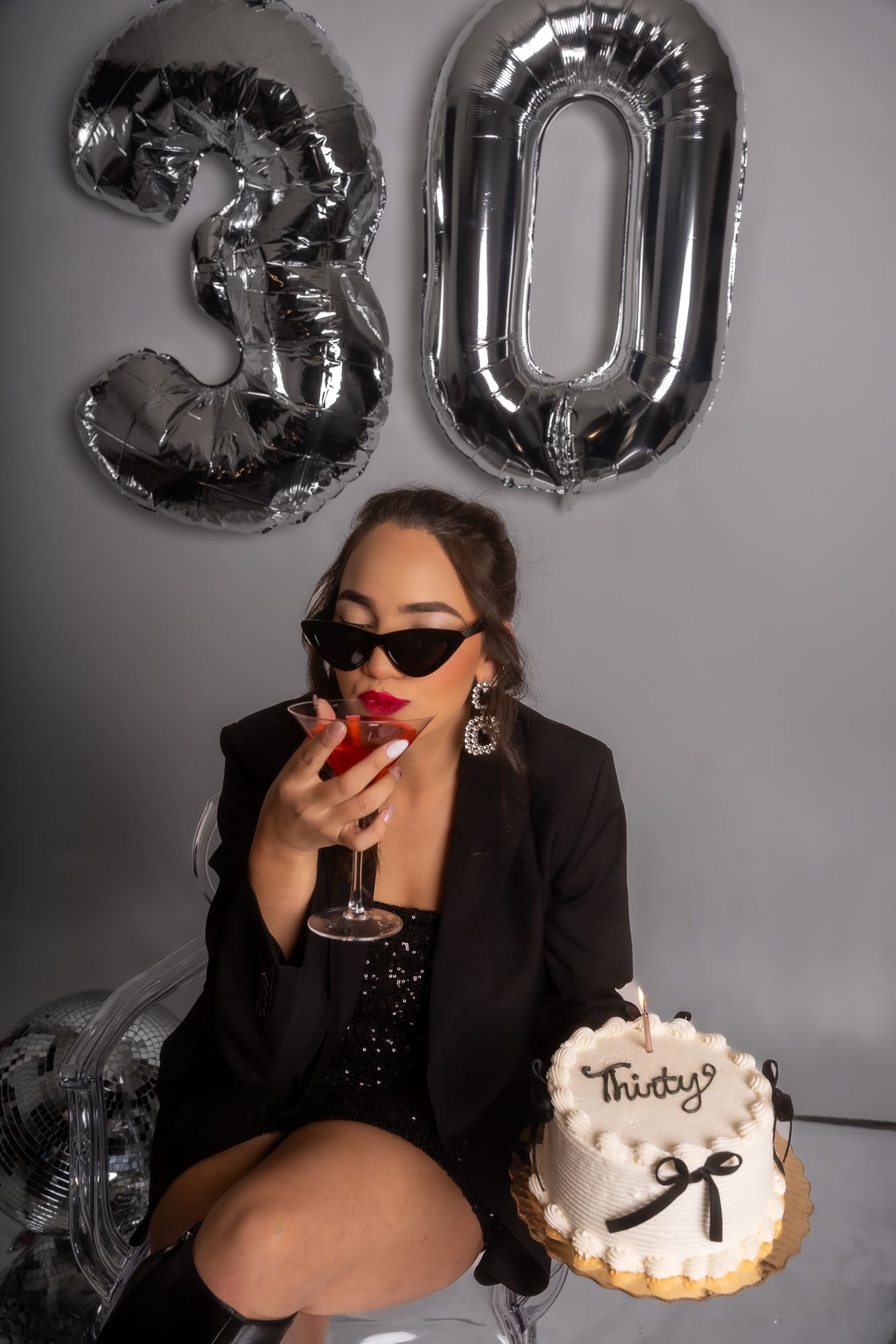 Chic birthday celebration with metallic balloons, red cocktail and white cake reading 'Thirty'.