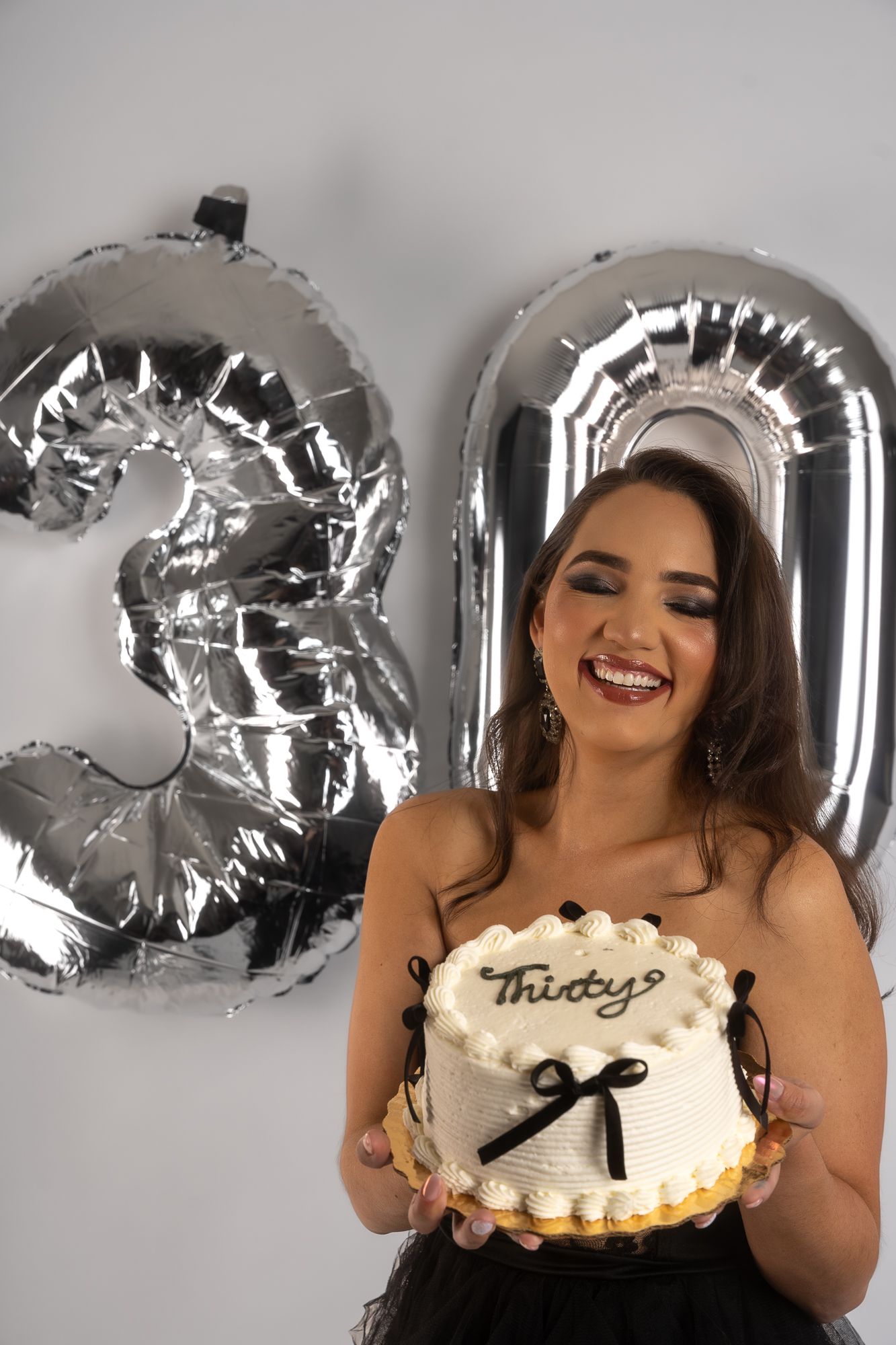 Celebration scene with silver balloons and birthday cake against light background.