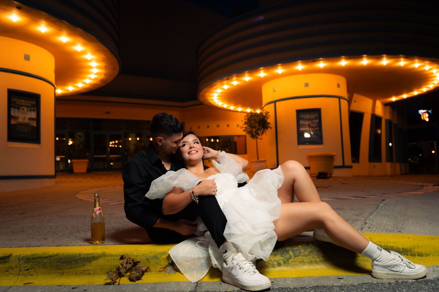 A playful nighttime couple photo with illuminated buildings in the background.