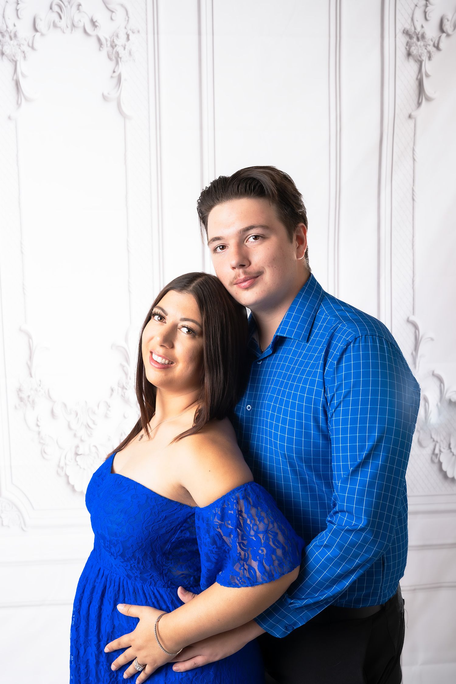 A joyful maternity portrait featuring a couple in coordinating blue outfits.