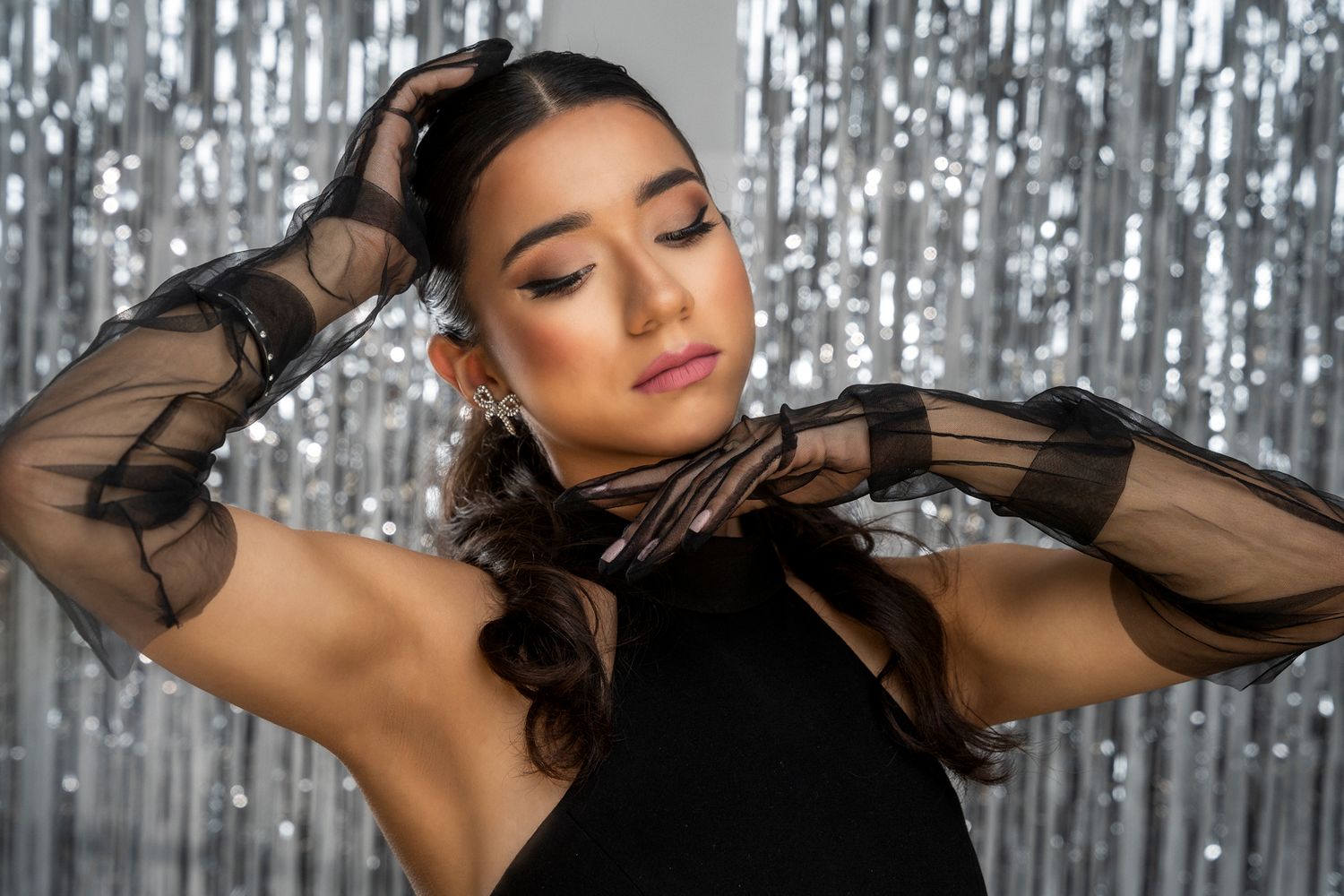 Elegant fashion pose against sparkly backdrop featuring black halter dress with sheer sleeves.