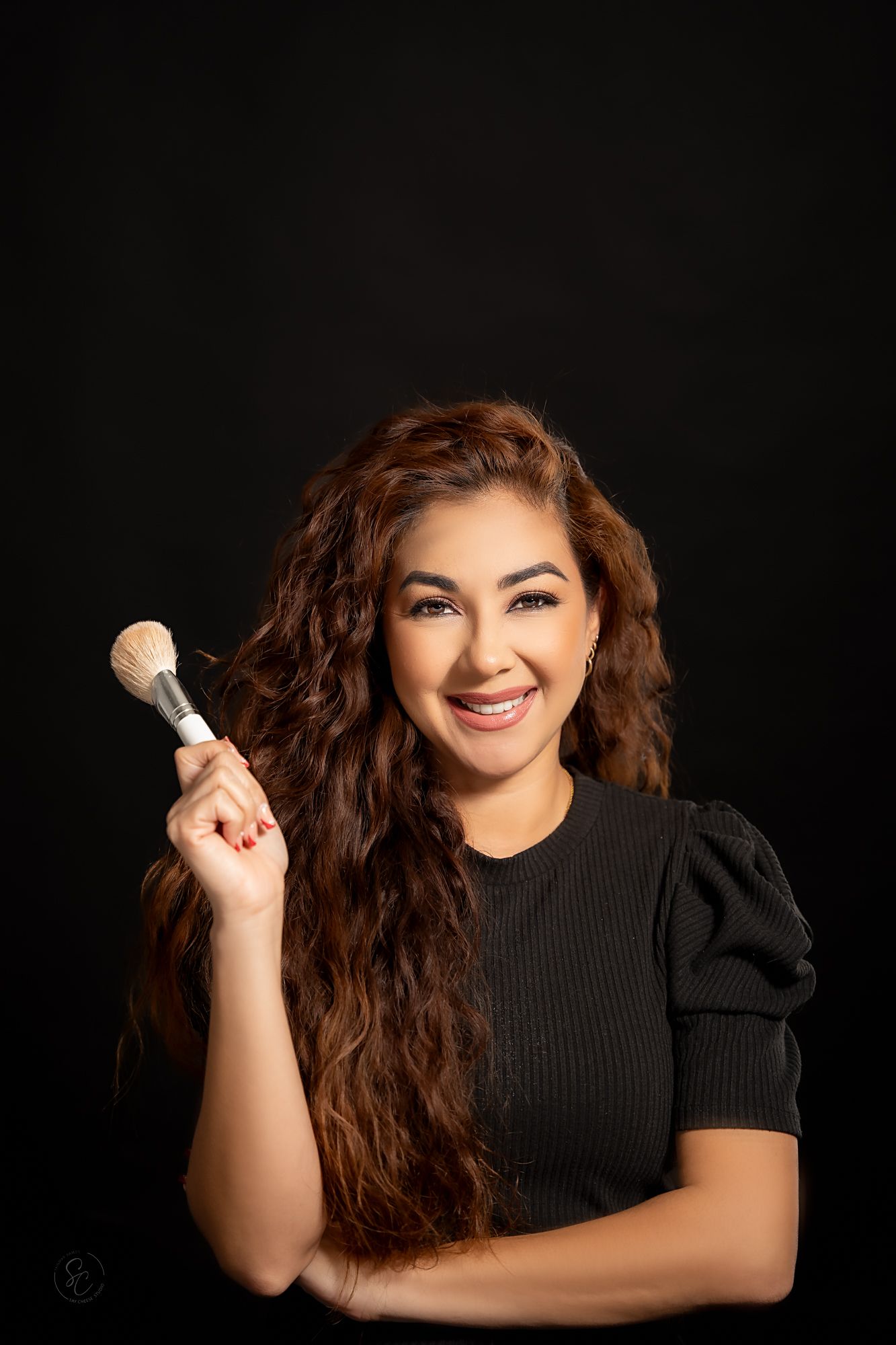 Person with flowing brown hair poses joyfully with styling products against black background.