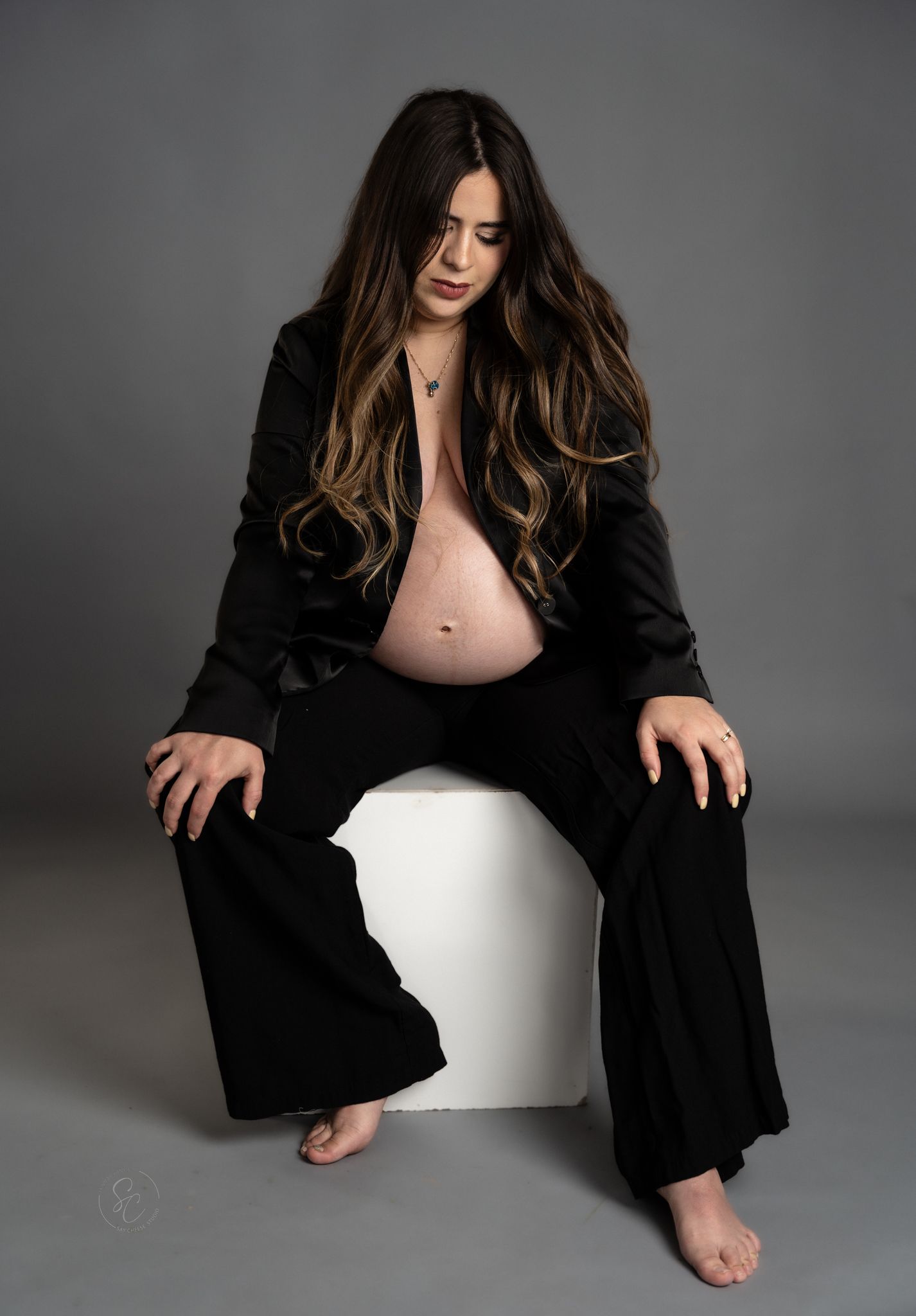 Artistic maternity portraits featuring a black blazer and white backdrop in moody lighting.