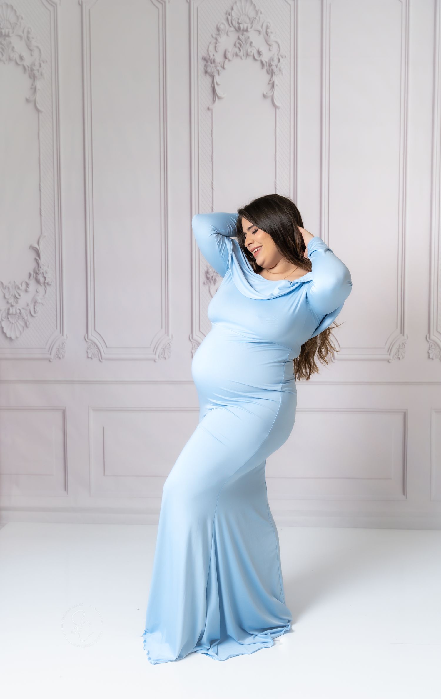 Maternity photo series showing graceful movement in a flowing light blue dress against a white backdrop.