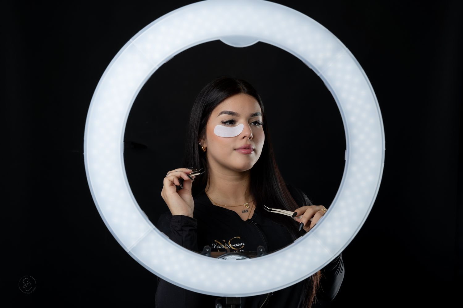 Portrait framed by circular ring light showing a person in dark clothing against black background.