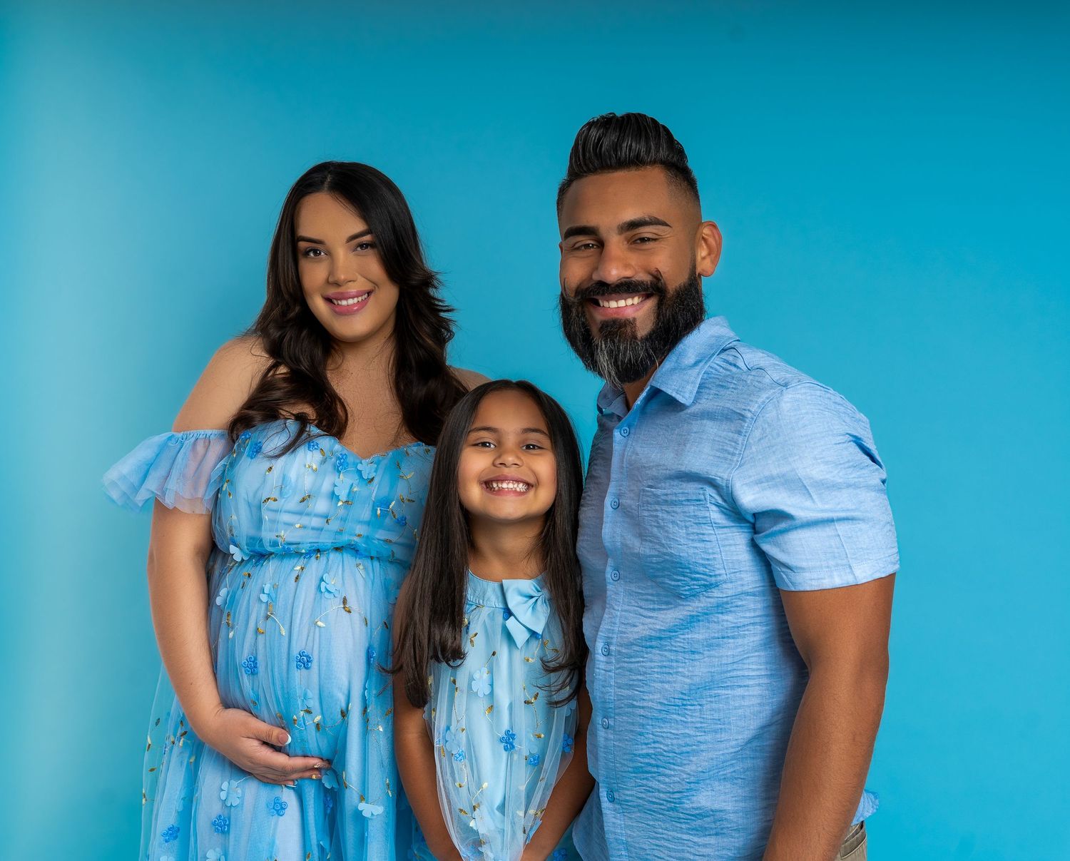 Couple poses in coordinating blue outfits against turquoise backdrop in romantic photoshoot series.